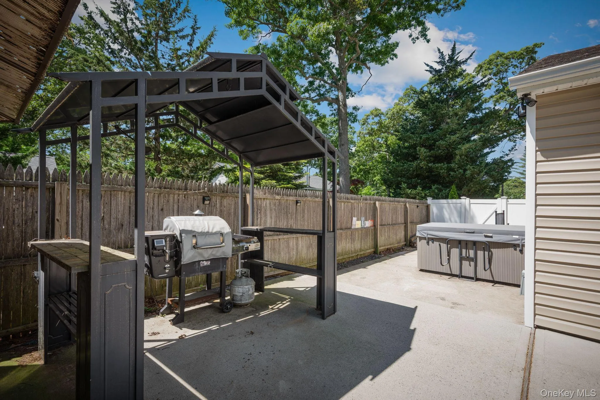 Paved patio area featuring a metal gazebo covering a BBQ area, a built-in outdoor bar, and a hot tub Paved patio area featuring a metal gazebo covering a BBQ area, a built-in outdoor bar, and a hot tub