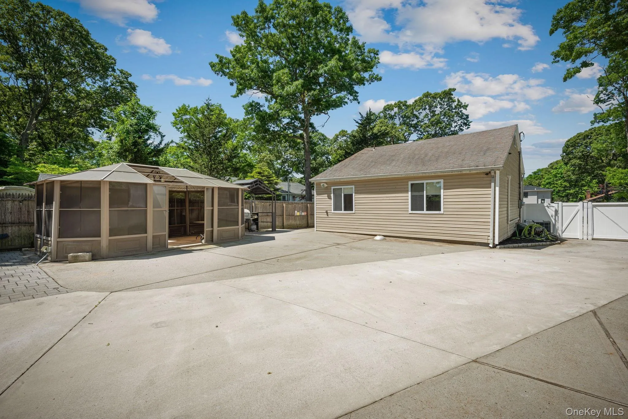 Concrete and paver patio behind house with a metal gazebo covering a BBQ area and a large screened in gazebo Concrete and paver patio behind house with a metal gazebo covering a BBQ area and a large screened in gazebo