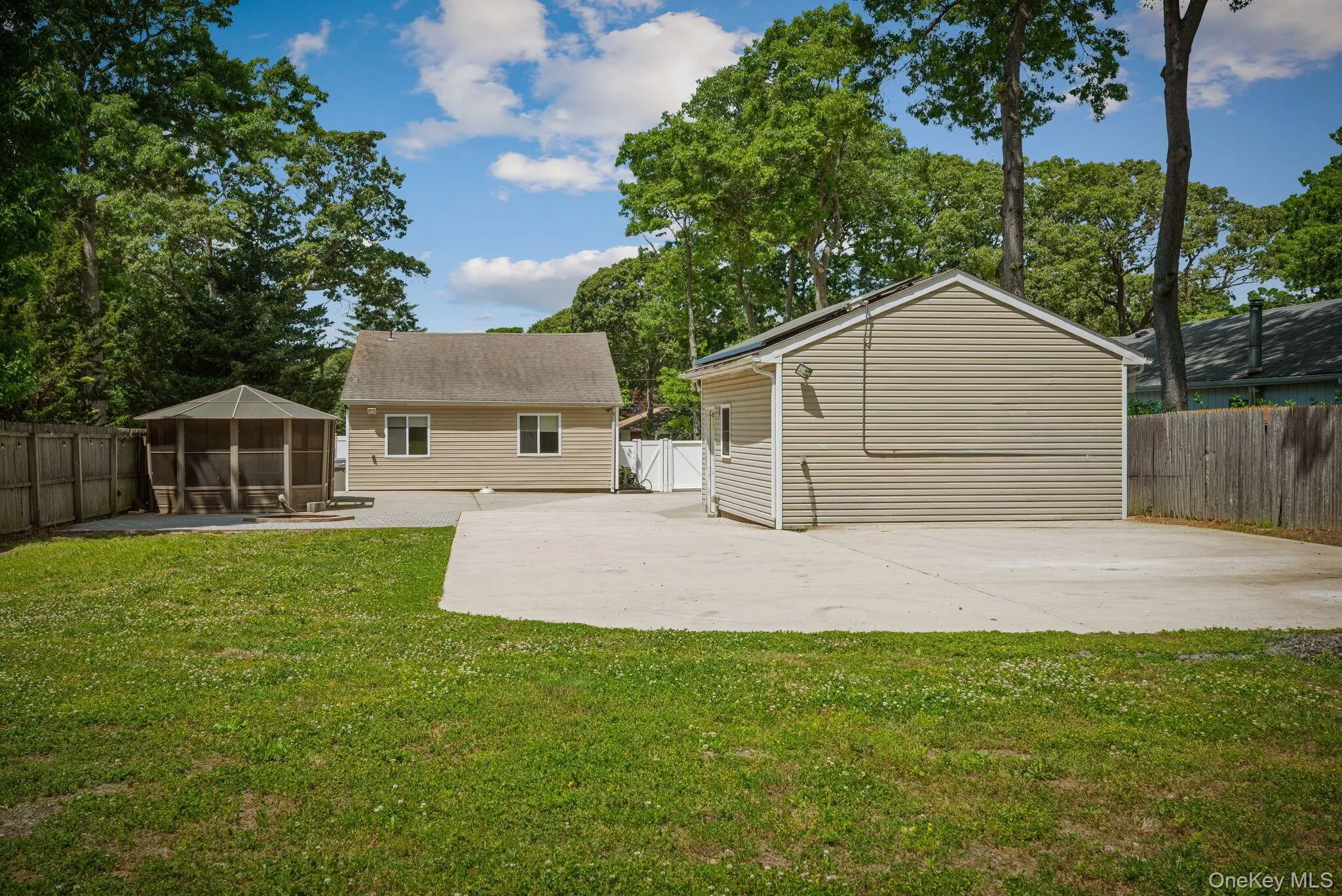 Spacious backyard with a large concrete patio, manicured lawn, and mature trees Spacious backyard with a large concrete patio, manicured lawn, and mature trees