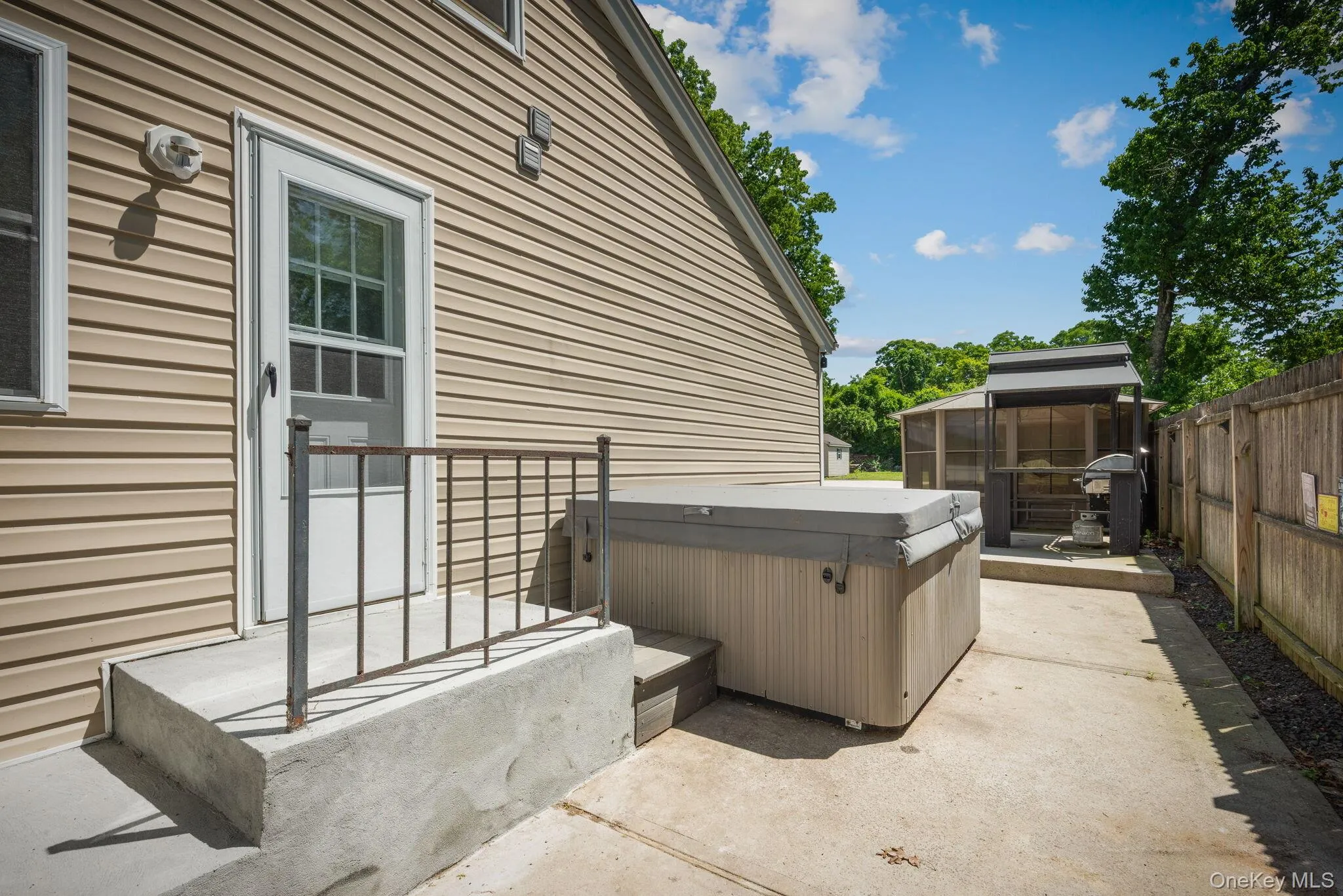 Entrance to side of the house with a private concrete patio featuring a hot tub, metal gazebo, and wood privacy fencing Entrance to side of the house with a private concrete patio featuring a hot tub, metal gazebo, and wood privacy fencing