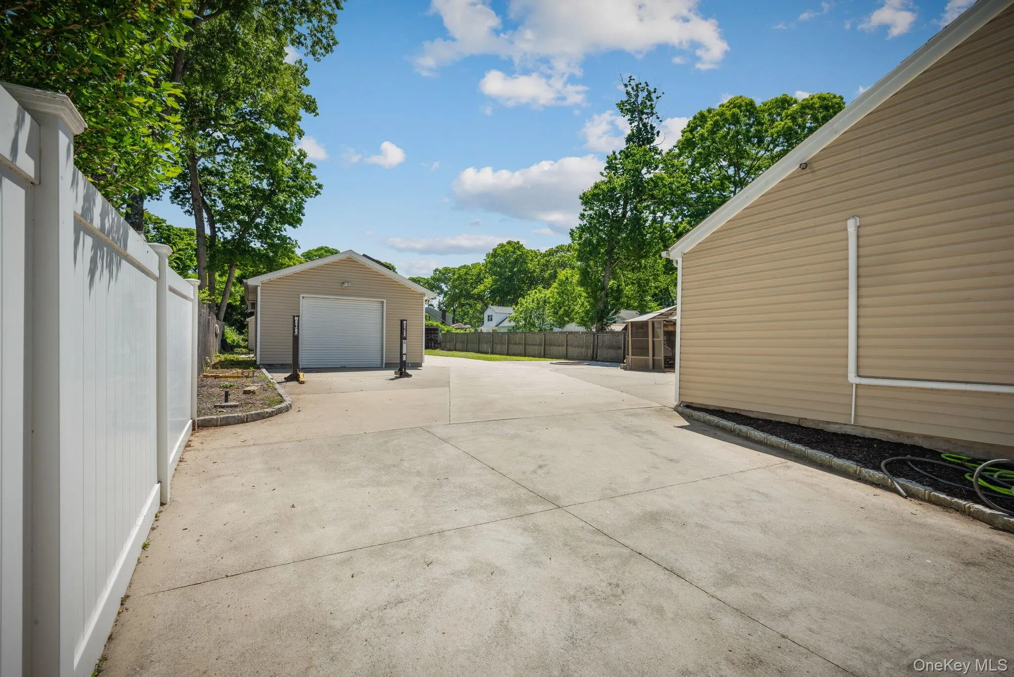 Concrete leading to the detached one-car garage with tan siding and white roll-up door Concrete leading to the detached one-car garage with tan siding and white roll-up door