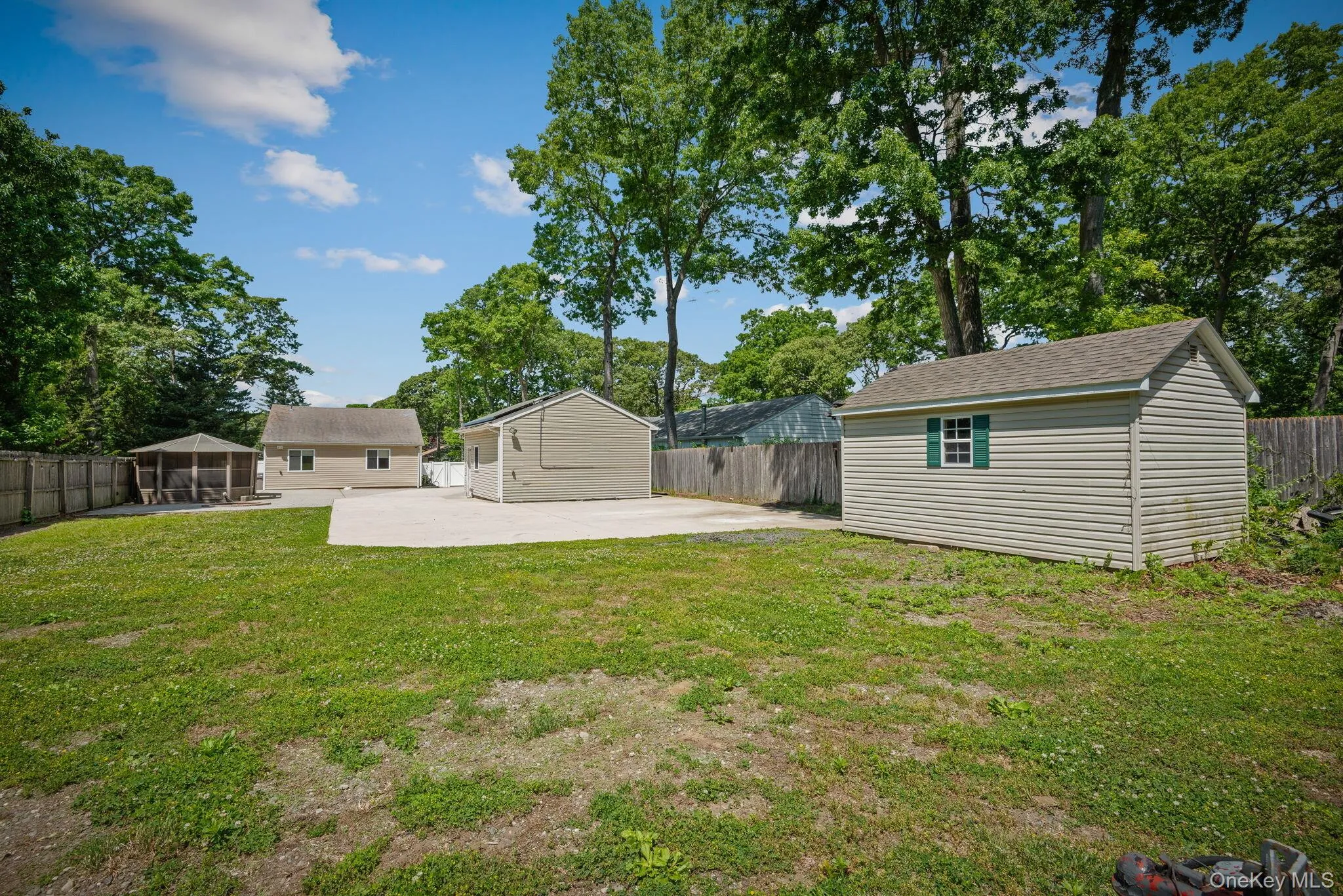Expansive rear property featuring a detached shed with green shutters, a concrete patio area, and a gazebo with a screened enclosure Expansive rear property featuring a detached shed with green shutters, a concrete patio area, and a gazebo with a screened enclosure