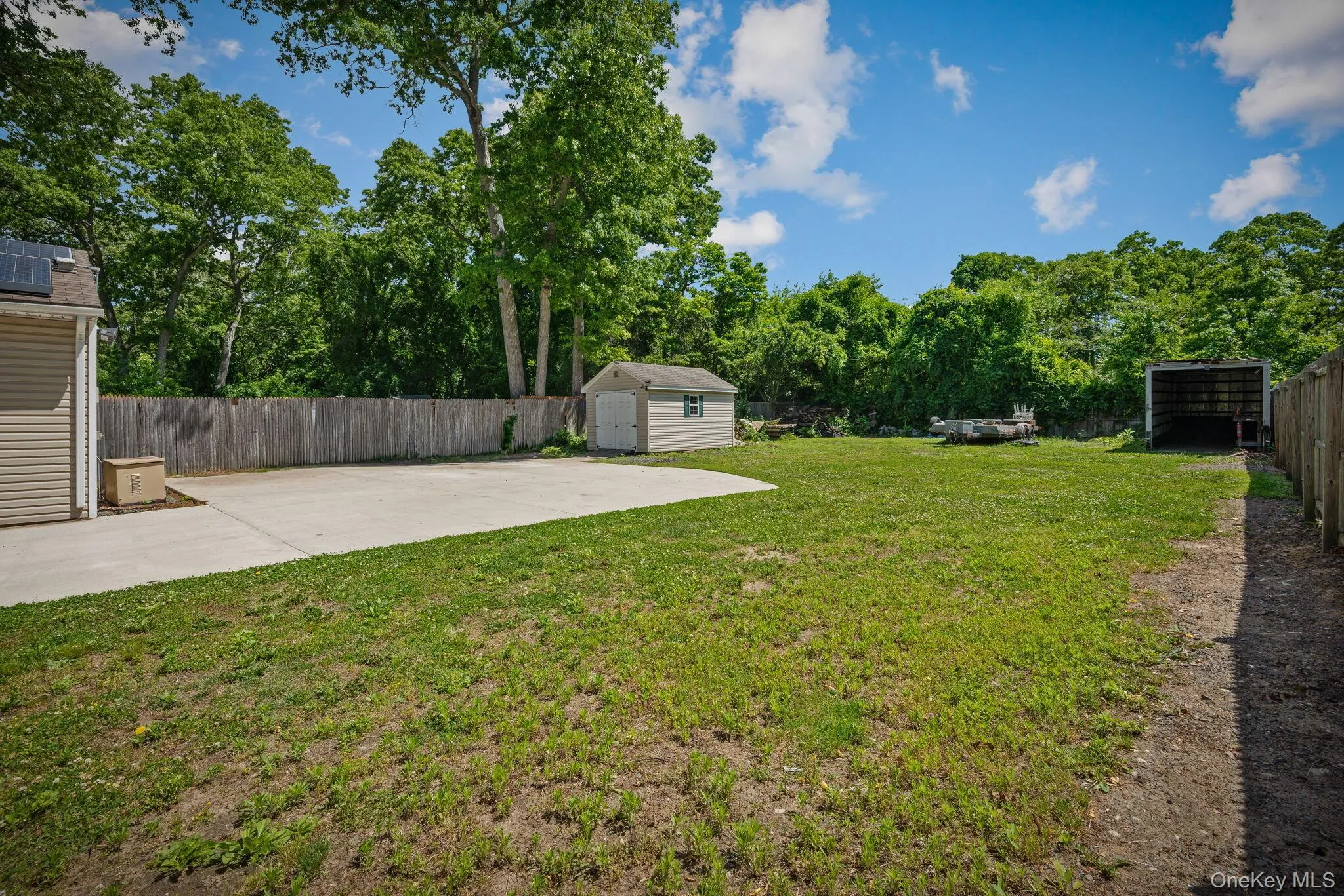 Expansive yard featuring a large concrete patio, mature perimeter trees, wood privacy fencing, and a detached shed Expansive yard featuring a large concrete patio, mature perimeter trees, wood privacy fencing, and a detached shed