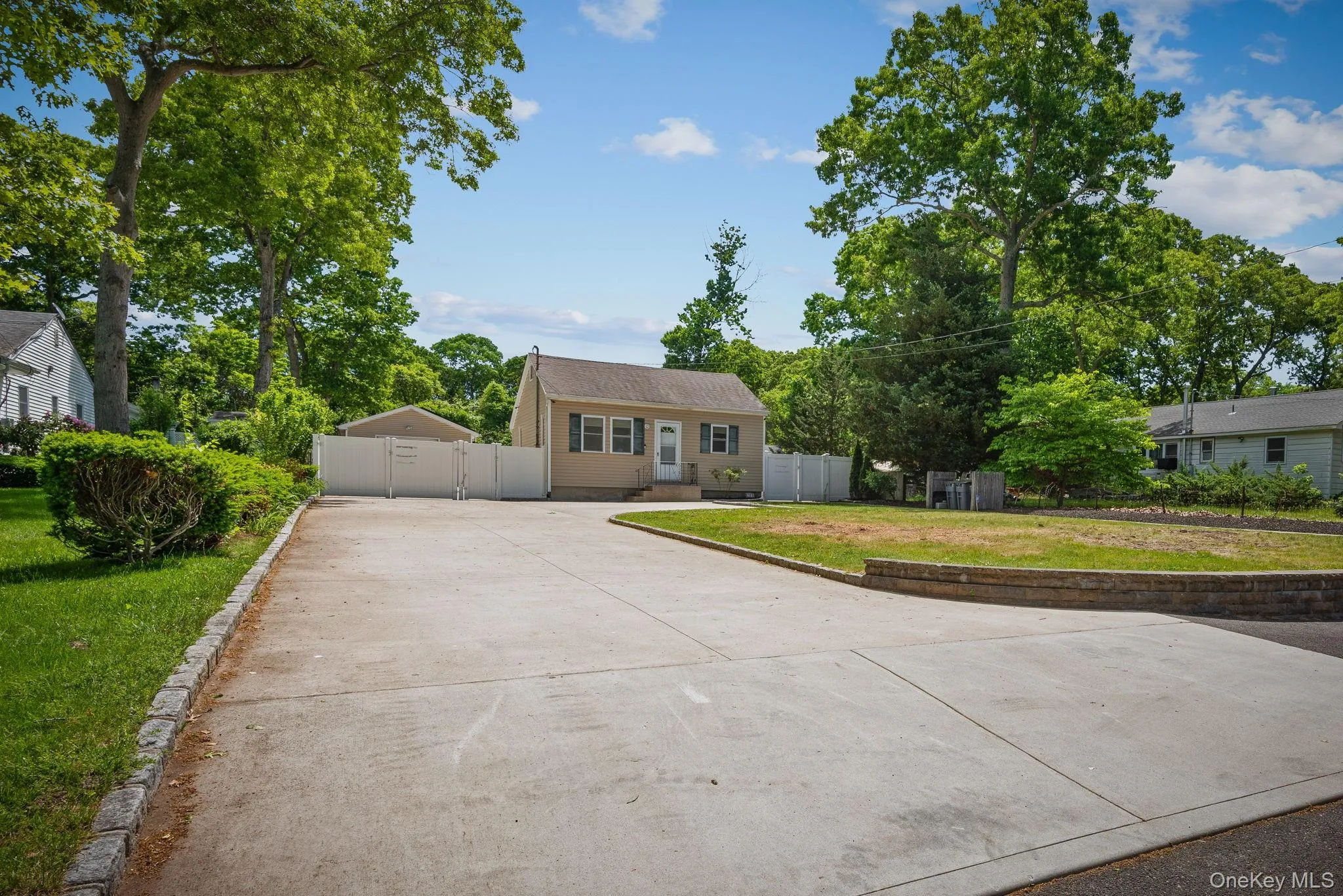 Single-story residence featuring light-colored siding with green shutters and a dark brown gabled roof with an expansive concrete driveway Single-story residence featuring light-colored siding with green shutters and a dark brown gabled roof with an expansive concrete driveway