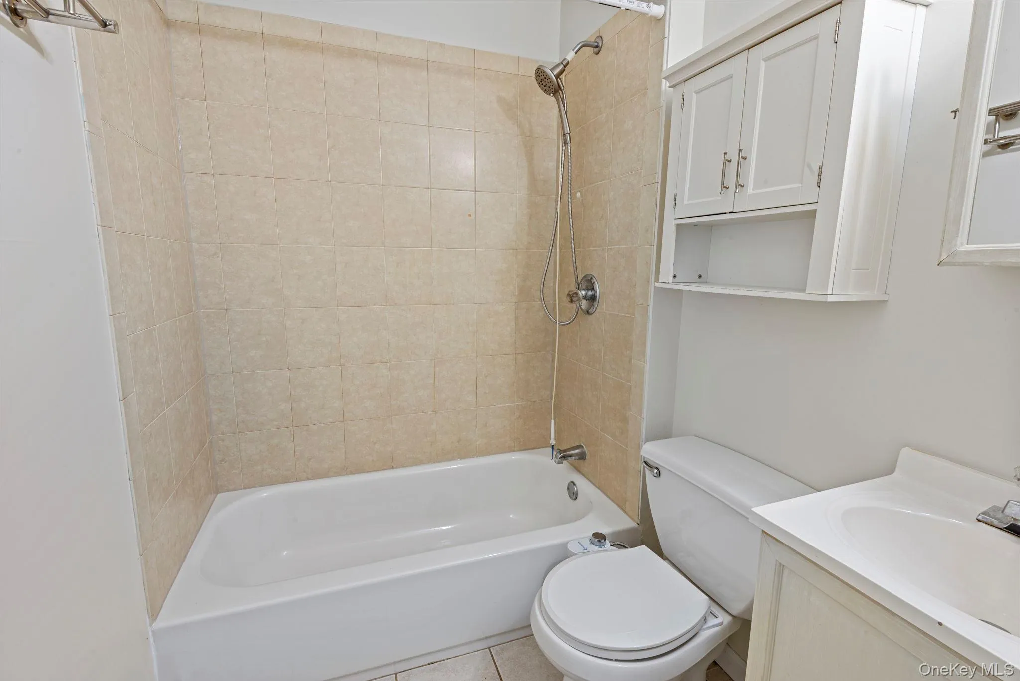 Bathroom featuring a tiled shower/tub combination with a handheld showerhead, white toilet, vanity with integrated sink, and white wall-mounted cabinetry Bathroom featuring a tiled shower/tub combination with a handheld showerhead, white toilet, vanity with integrated sink, and white wall-mounted cabinetry