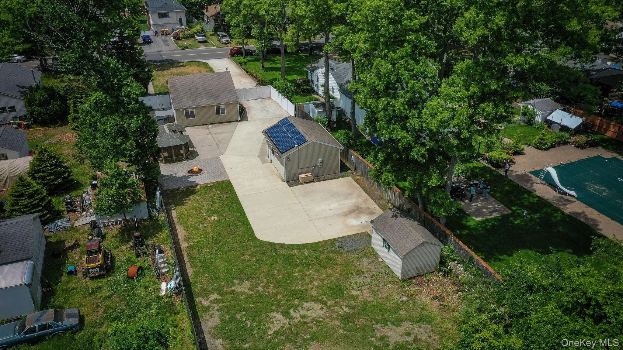 Aerial property view of expansive paved driveway leading to a single-story dwelling with a tan siding exterior, green shutters, white PVC fence Aerial property view of expansive paved driveway leading to a single-story dwelling with a tan siding exterior, green shutters, white PVC fence