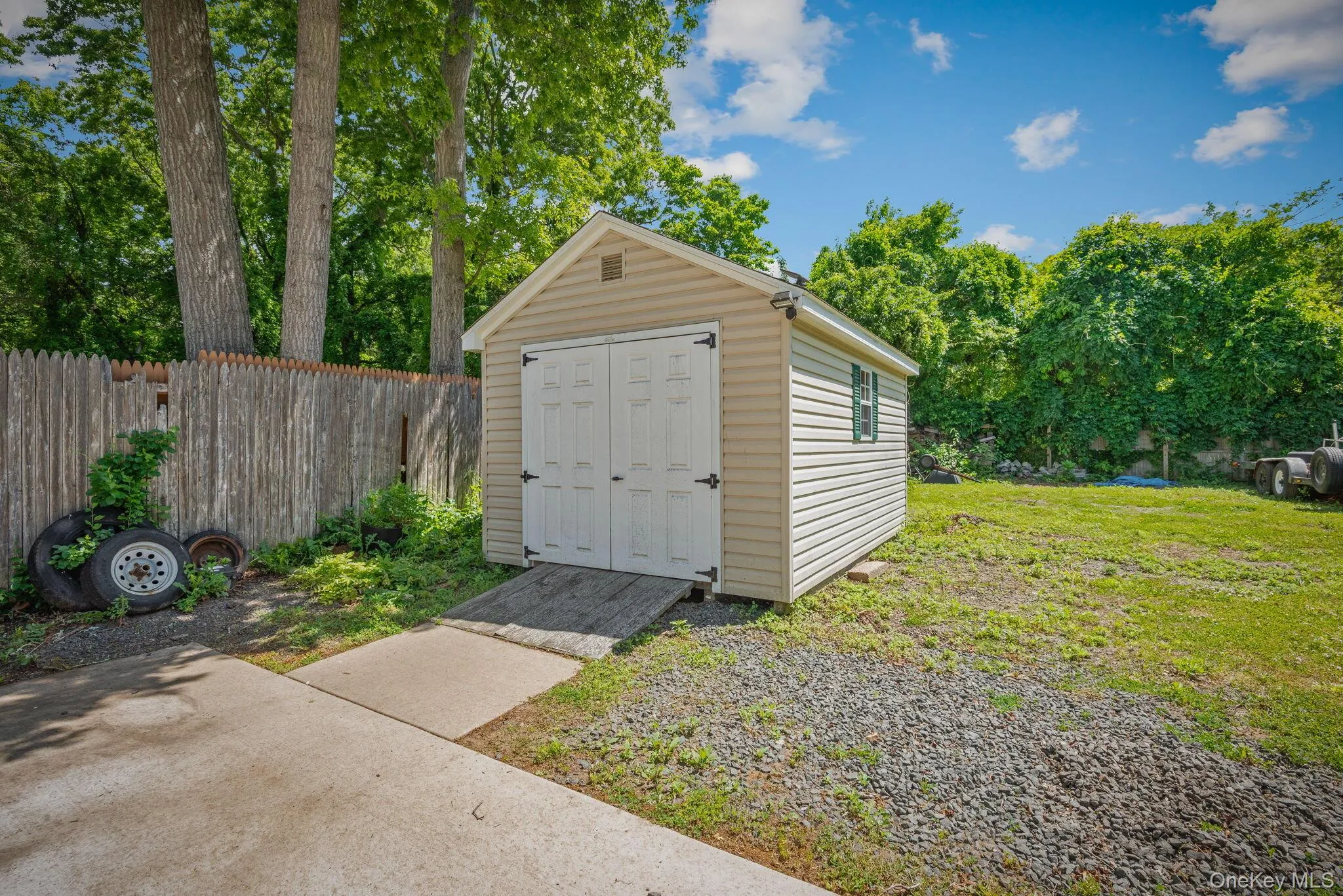 Freestanding storage shed featuring tan siding, white double doors with black hardware, and a small green-trimmed window Freestanding storage shed featuring tan siding, white double doors with black hardware, and a small green-trimmed window