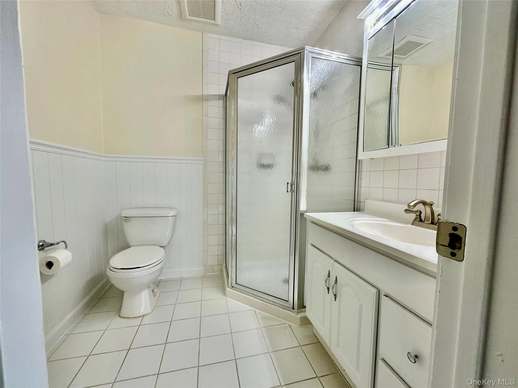 Bathroom featuring a shower with door, tile patterned flooring, vanity, a textured ceiling, and toilet Bathroom featuring a shower with door, tile patterned flooring, vanity, a textured ceiling, and toilet