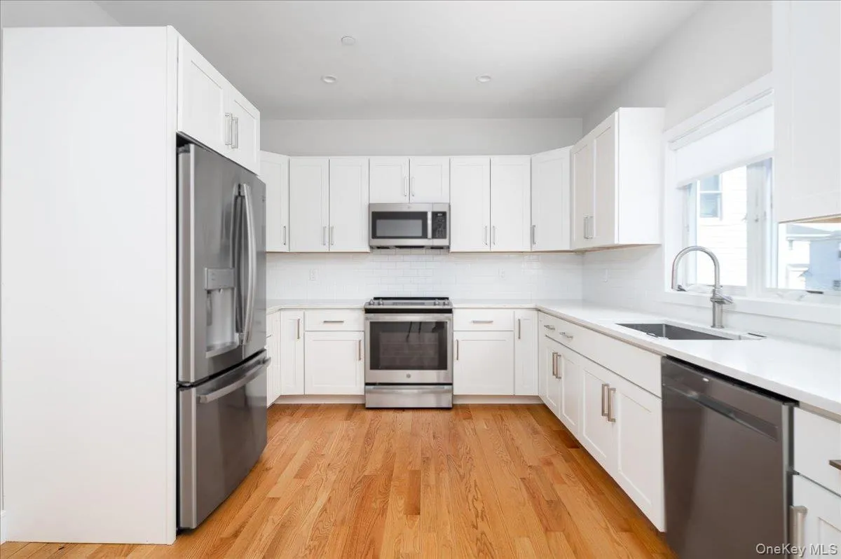 Kitchen featuring decorative backsplash, white cabinets, light countertops, stainless steel appliances, and a sink Kitchen featuring decorative backsplash, white cabinets, light countertops, stainless steel appliances, and a sink