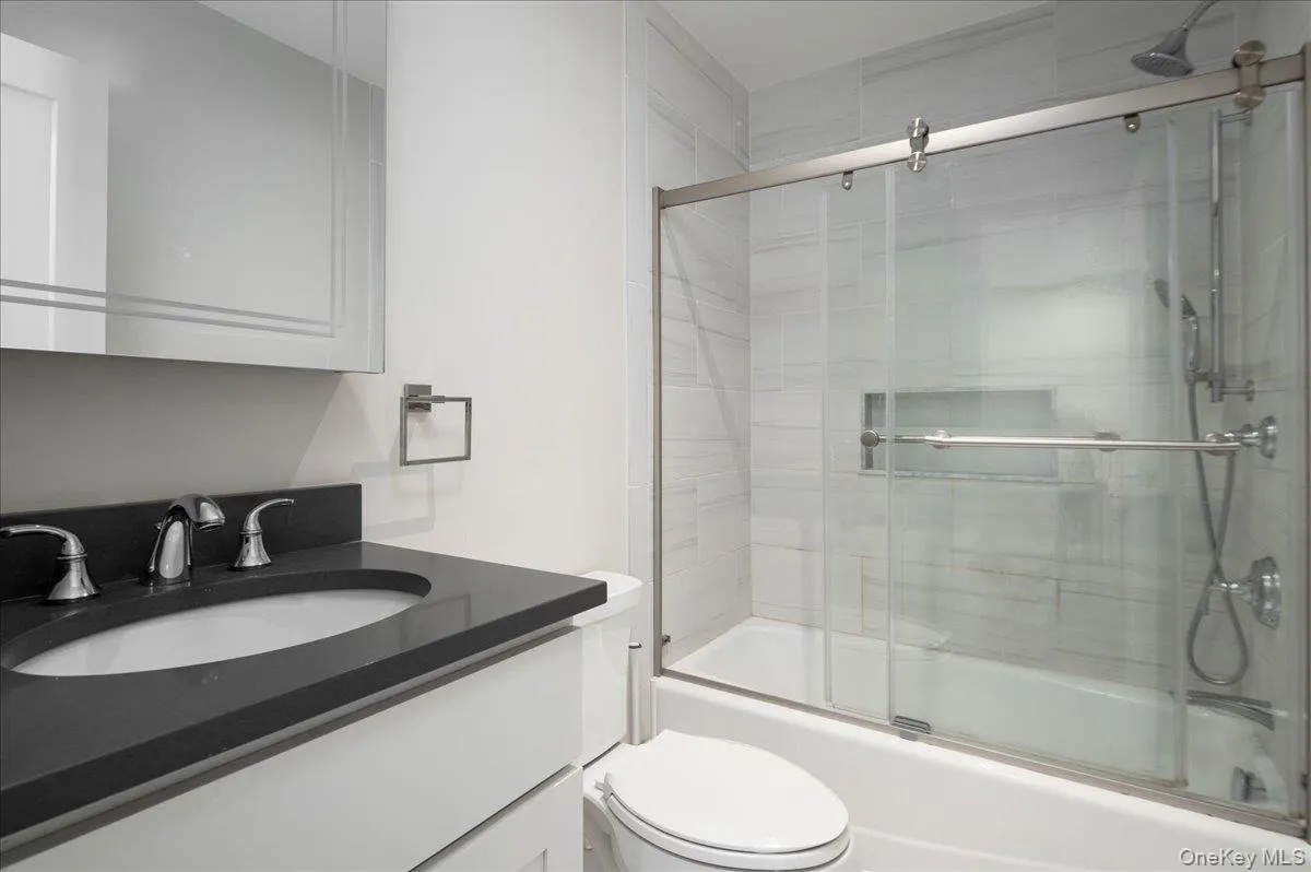 Full bathroom with toilet, vanity, and shower / bath combination with glass door Full bathroom with toilet, vanity, and shower / bath combination with glass door