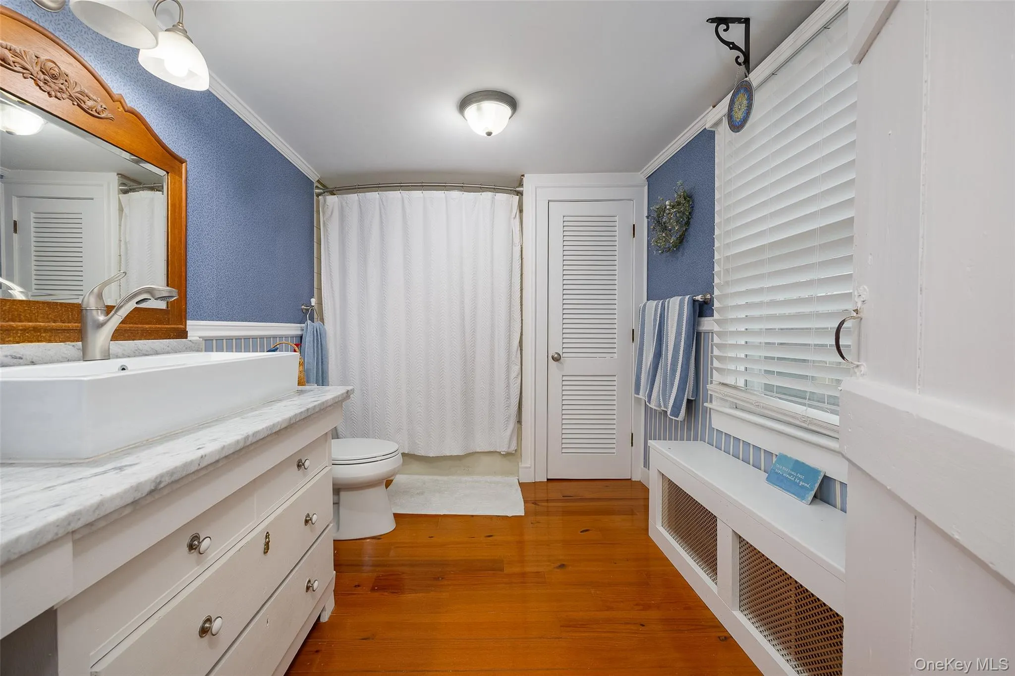 Full bathroom with radiator heating unit, vanity, light wood finished floors, ornamental molding, and a textured wall Full bathroom with radiator heating unit, vanity, light wood finished floors, ornamental molding, and a textured wall