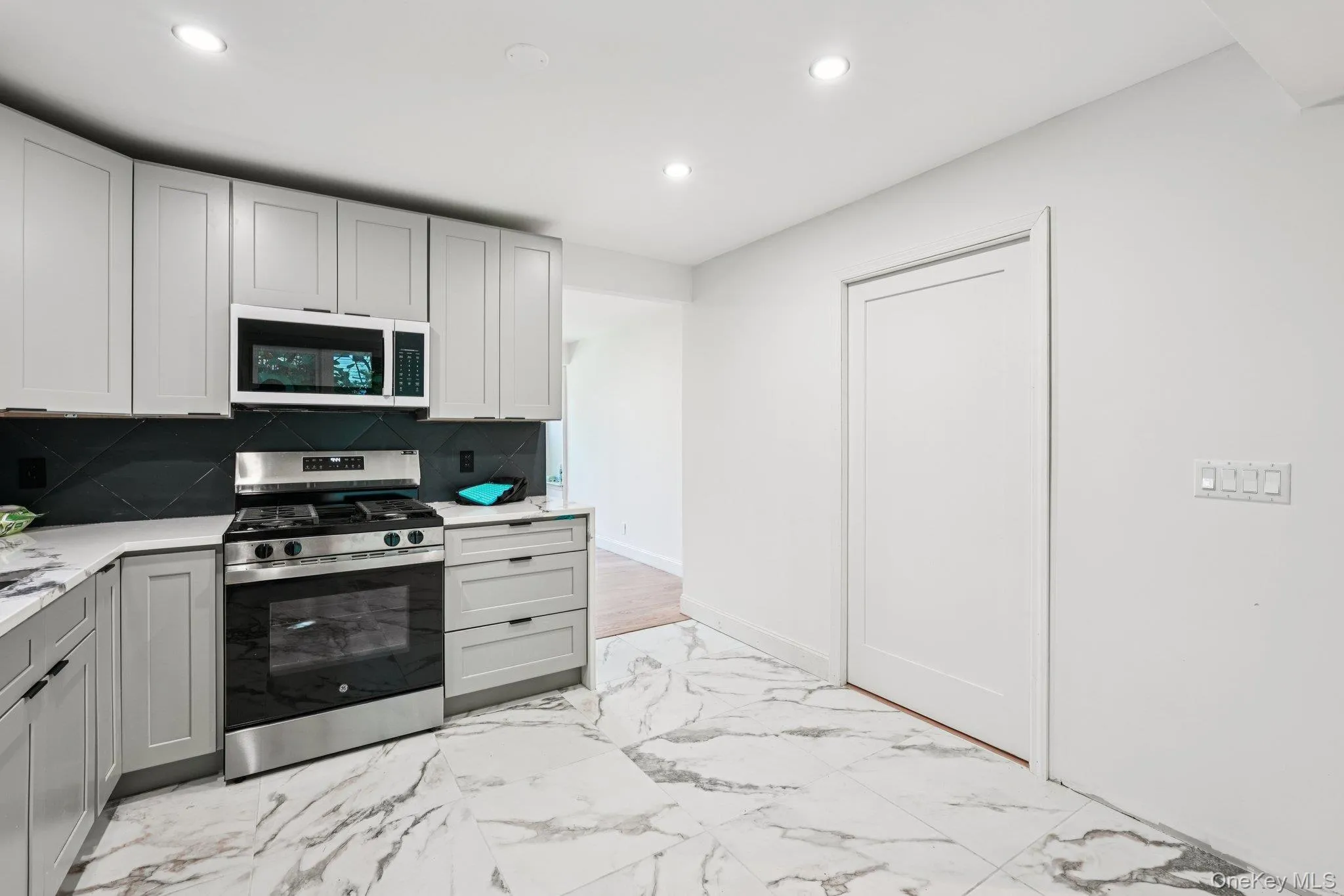 Kitchen featuring white microwave, stainless steel range with gas stovetop, recessed lighting, light marbled flooring, and light countertops Kitchen featuring white microwave, stainless steel range with gas stovetop, recessed lighting, light marbled flooring, and light countertops
