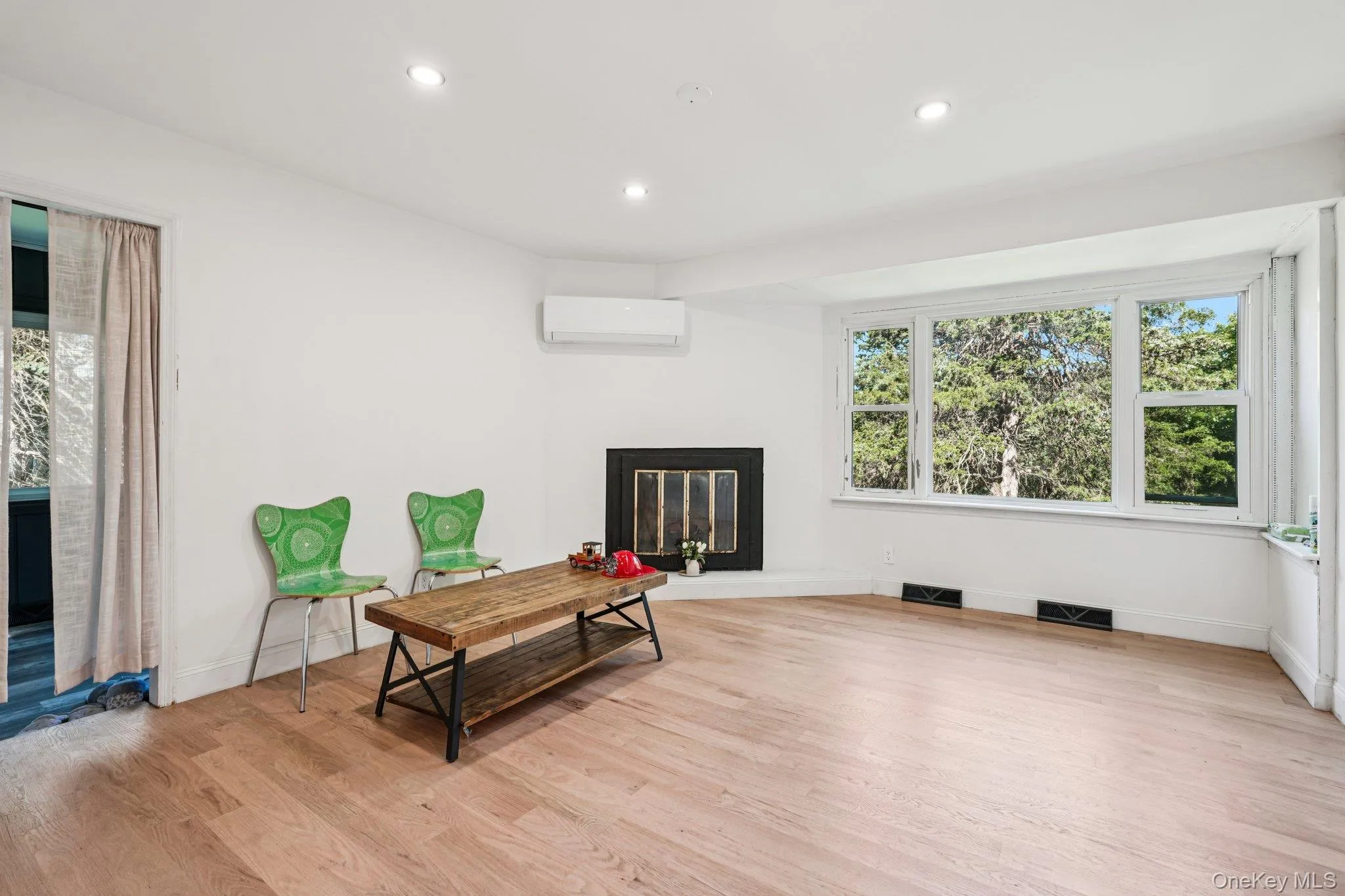 Living area featuring a glass covered fireplace, a wall mounted air conditioner, light wood finished floors, and recessed lighting Living area featuring a glass covered fireplace, a wall mounted air conditioner, light wood finished floors, and recessed lighting