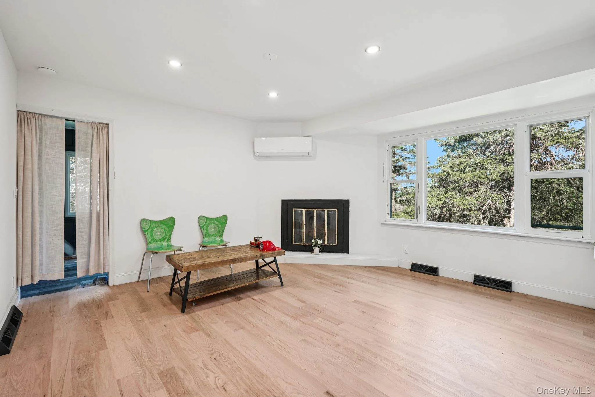 Living area with a wall mounted mini split AC/heat unit, a glass covered fireplace, light wood-style floors, and recessed lighting Living area with a wall mounted mini split AC/heat unit, a glass covered fireplace, light wood-style floors, and recessed lighting