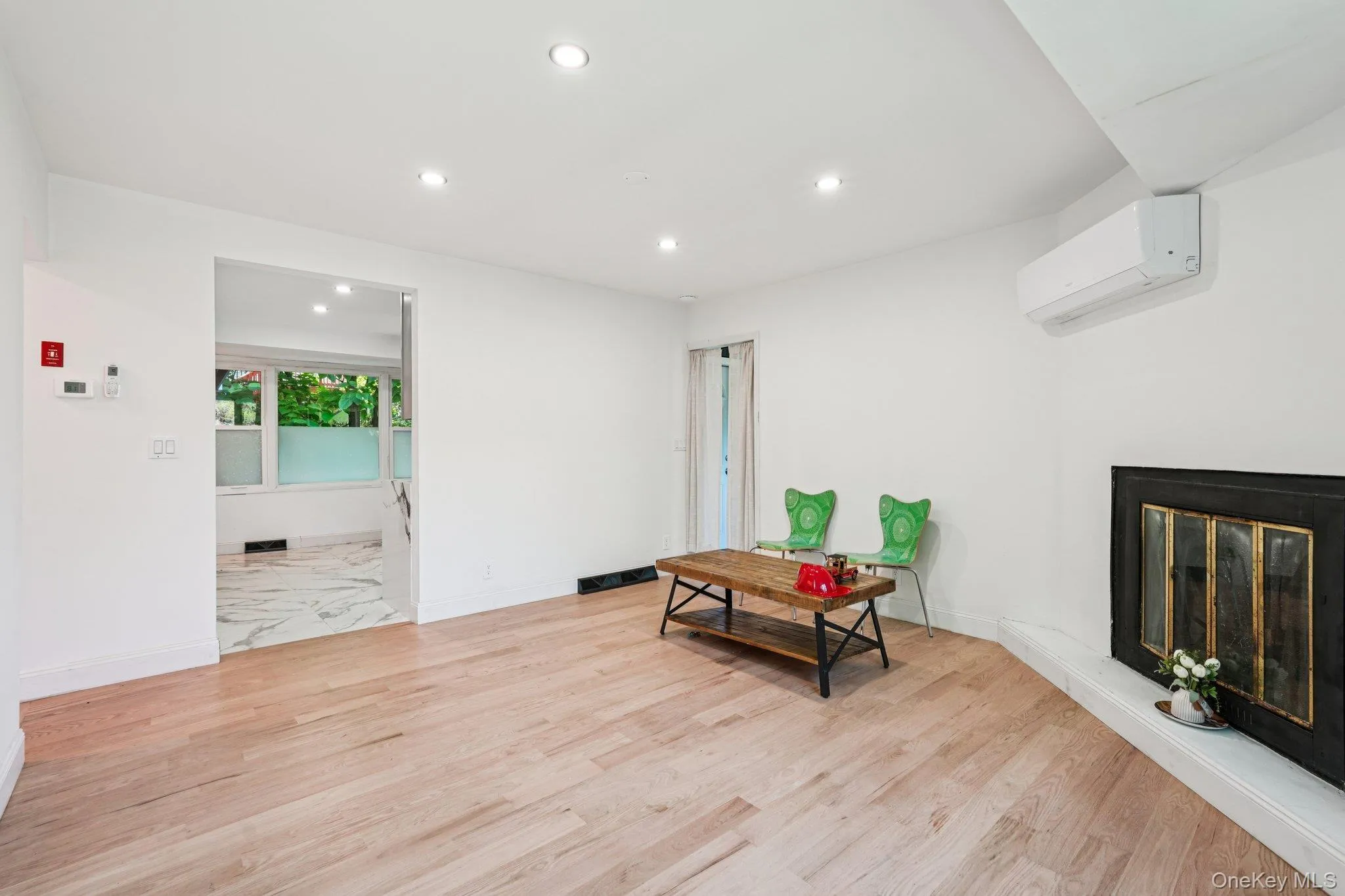 Living area with a mini split Heat/AC wall unit, recessed lighting, light wood finished floors, and a glass covered fireplace Living area with a mini split Heat/AC wall unit, recessed lighting, light wood finished floors, and a glass covered fireplace