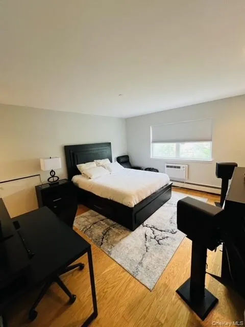 Bedroom with a wall mounted AC, baseboard heating, and hardwood / wood-style flooring Bedroom with a wall mounted AC, baseboard heating, and hardwood / wood-style flooring