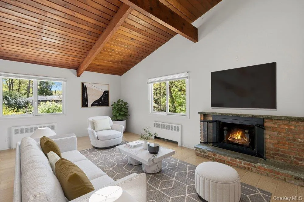 Vaulted wood-plank ceiling with exposed beams, brick fireplace with stone hearth, wood flooring, and multiple windows Vaulted wood-plank ceiling with exposed beams, brick fireplace with stone hearth, wood flooring, and multiple windows