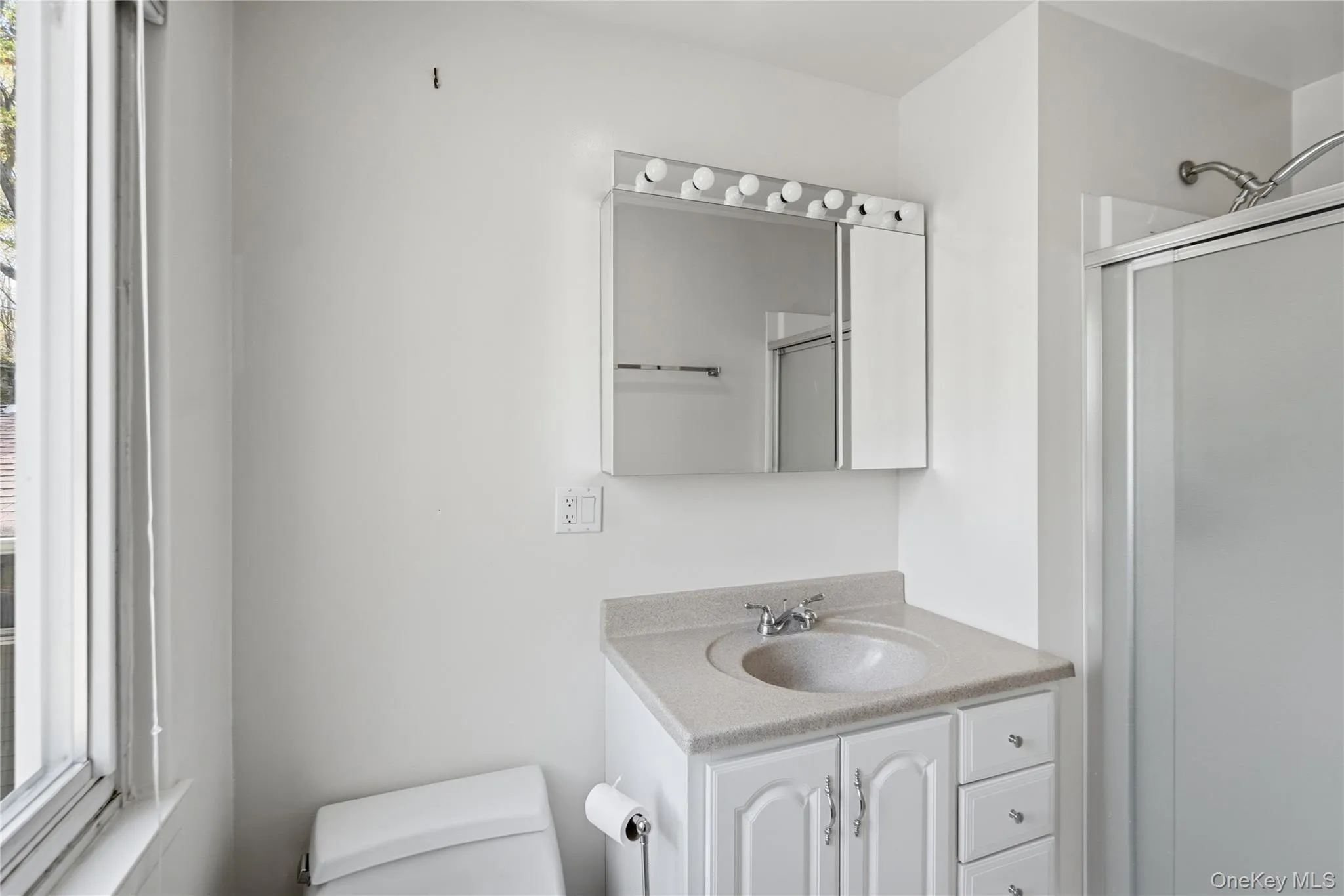 Bathroom featuring a white vanity with integrated sink, a medicine cabinet with vanity lighting, and a walk-in shower with a frosted glass door Bathroom featuring a white vanity with integrated sink, a medicine cabinet with vanity lighting, and a walk-in shower with a frosted glass door