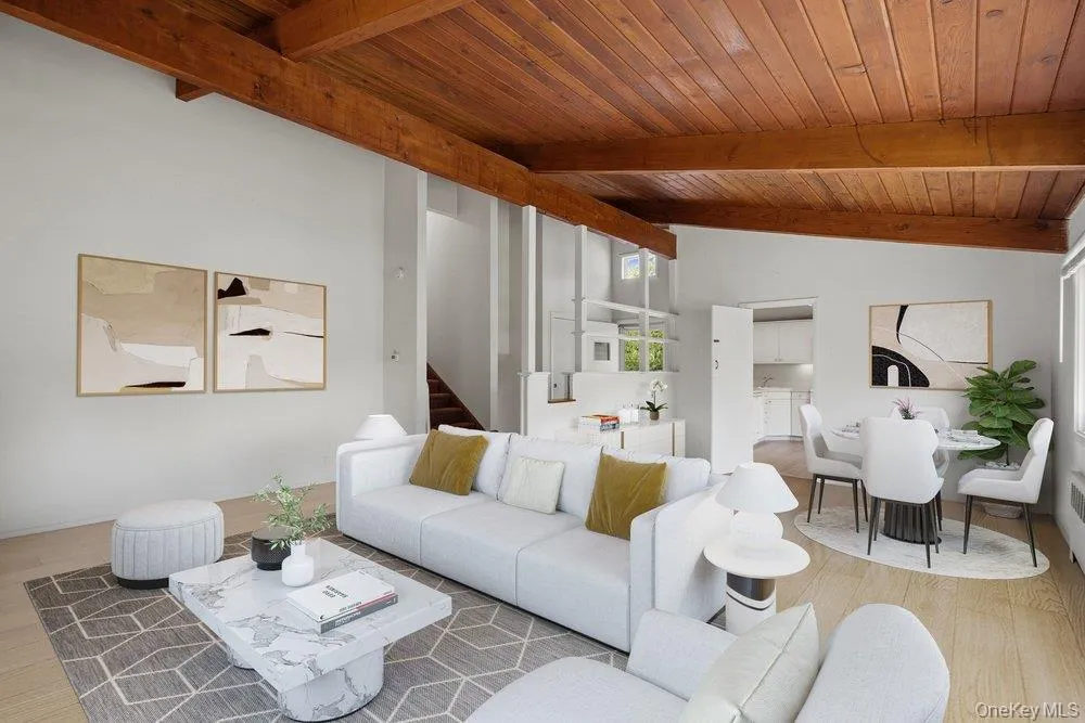 Open-concept living area featuring a wood-plank ceiling with exposed beams, wood flooring, and a dining area leading to kitchen Open-concept living area featuring a wood-plank ceiling with exposed beams, wood flooring, and a dining area leading to kitchen