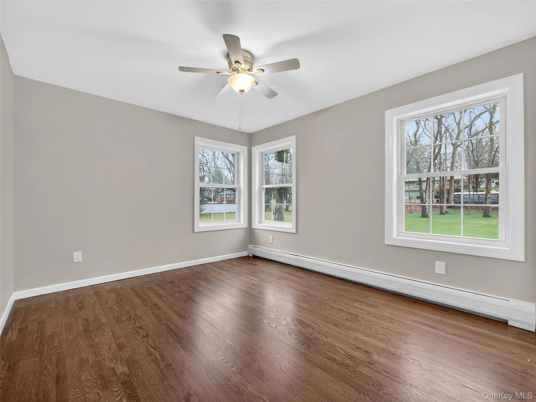 Spare room with a baseboard heating unit, dark wood-style flooring, and ceiling fan Spare room with a baseboard heating unit, dark wood-style flooring, and ceiling fan