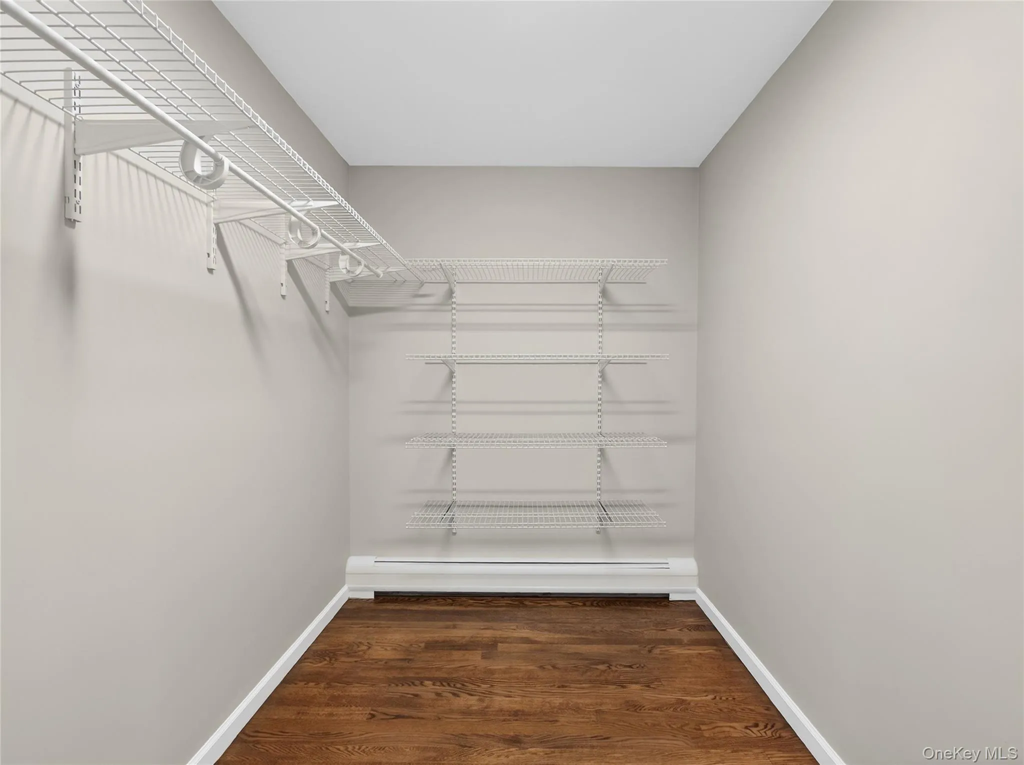 Walk in closet with dark wood finished floors and baseboard heating Walk in closet with dark wood finished floors and baseboard heating