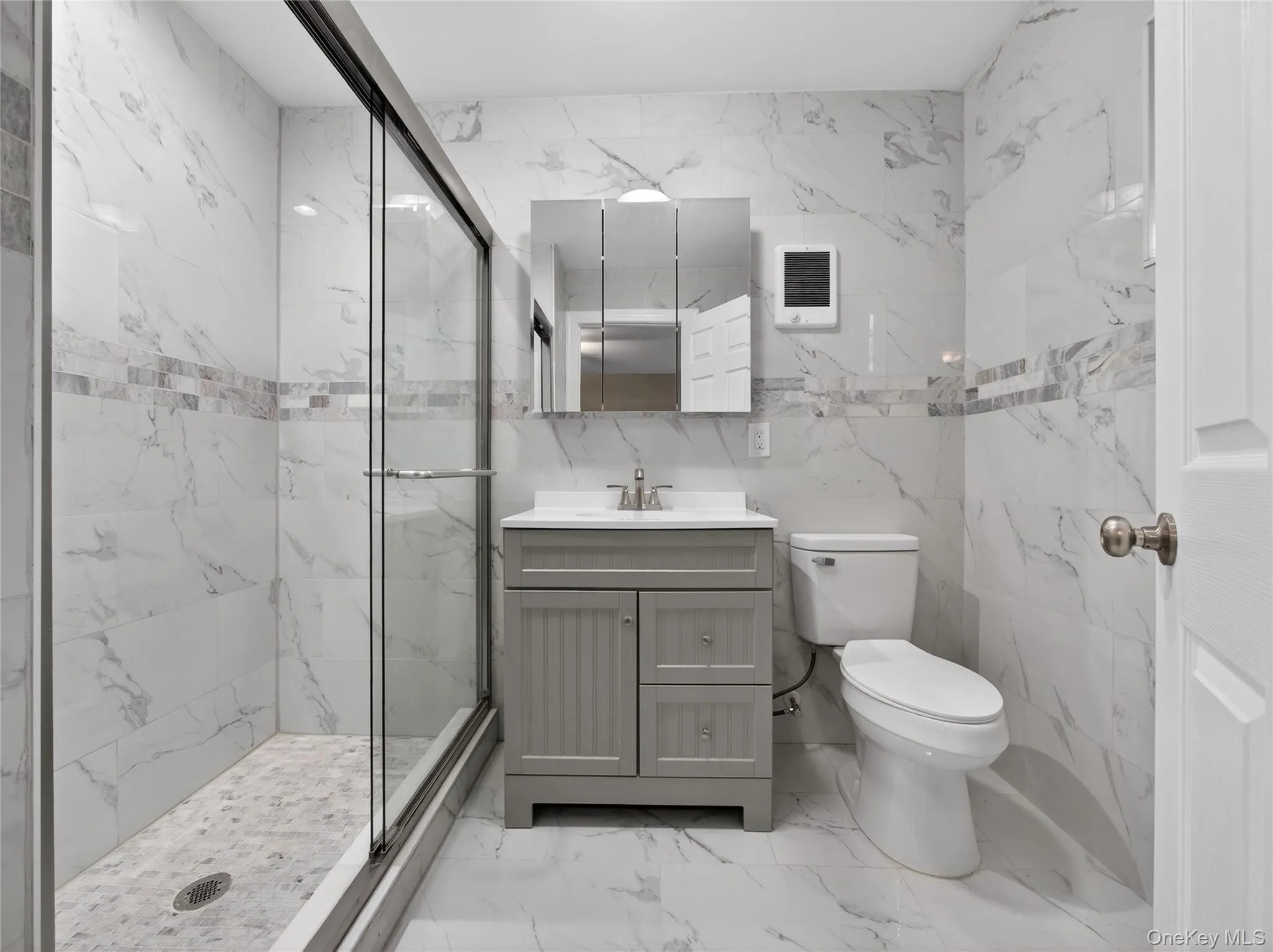 Bathroom with vanity, tile walls, a marble finish shower, light marble finish flooring, and heating unit Bathroom with vanity, tile walls, a marble finish shower, light marble finish flooring, and heating unit