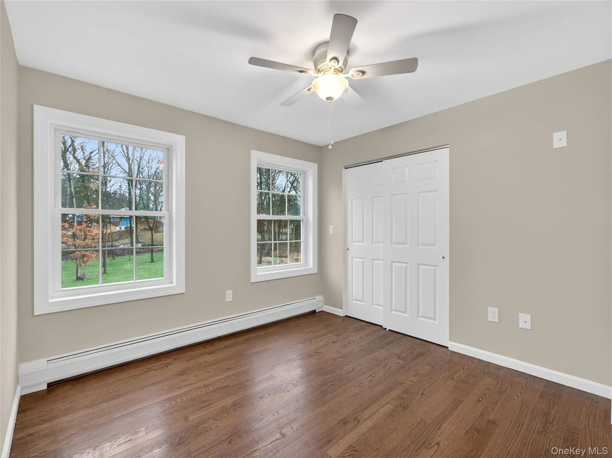 Unfurnished bedroom featuring a baseboard radiator, dark wood-style flooring, ceiling fan, and a closet Unfurnished bedroom featuring a baseboard radiator, dark wood-style flooring, ceiling fan, and a closet