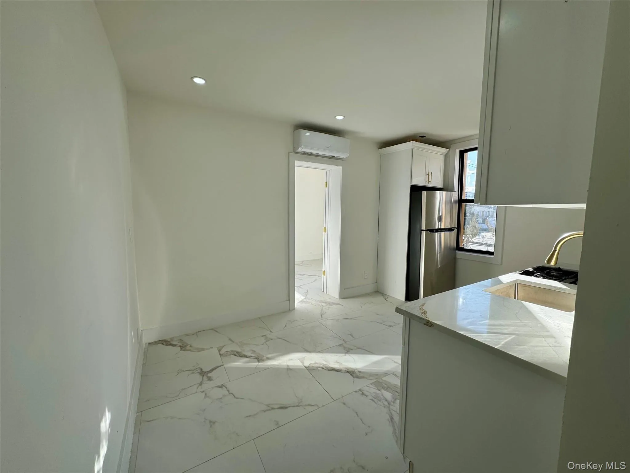 Kitchen with white cabinetry, kitchen peninsula, stainless steel refrigerator, and an AC wall unit Kitchen with white cabinetry, kitchen peninsula, stainless steel refrigerator, and an AC wall unit