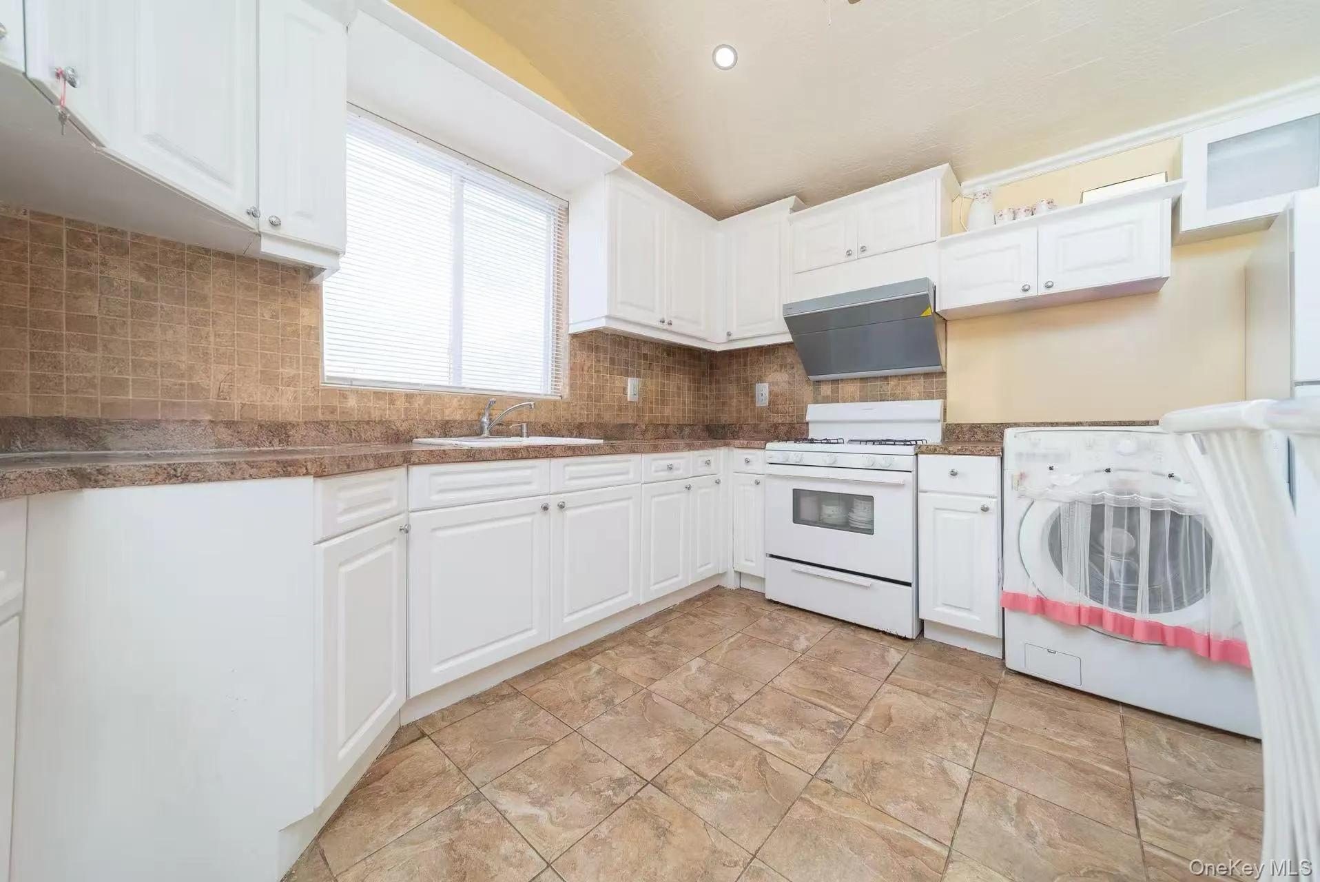 Kitchen with washer / clothes dryer, white gas stove, dark countertops, white cabinets, and recessed lighting Kitchen with washer / clothes dryer, white gas stove, dark countertops, white cabinets, and recessed lighting