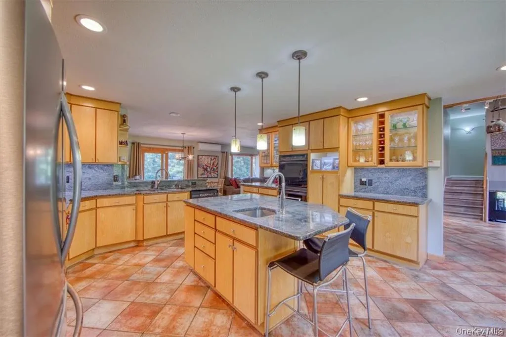 Stainless steel appliances, recessed lighting, wood-finish cabinetry, stone countertops, and a center island with bar seating Stainless steel appliances, recessed lighting, wood-finish cabinetry, stone countertops, and a center island with bar seating