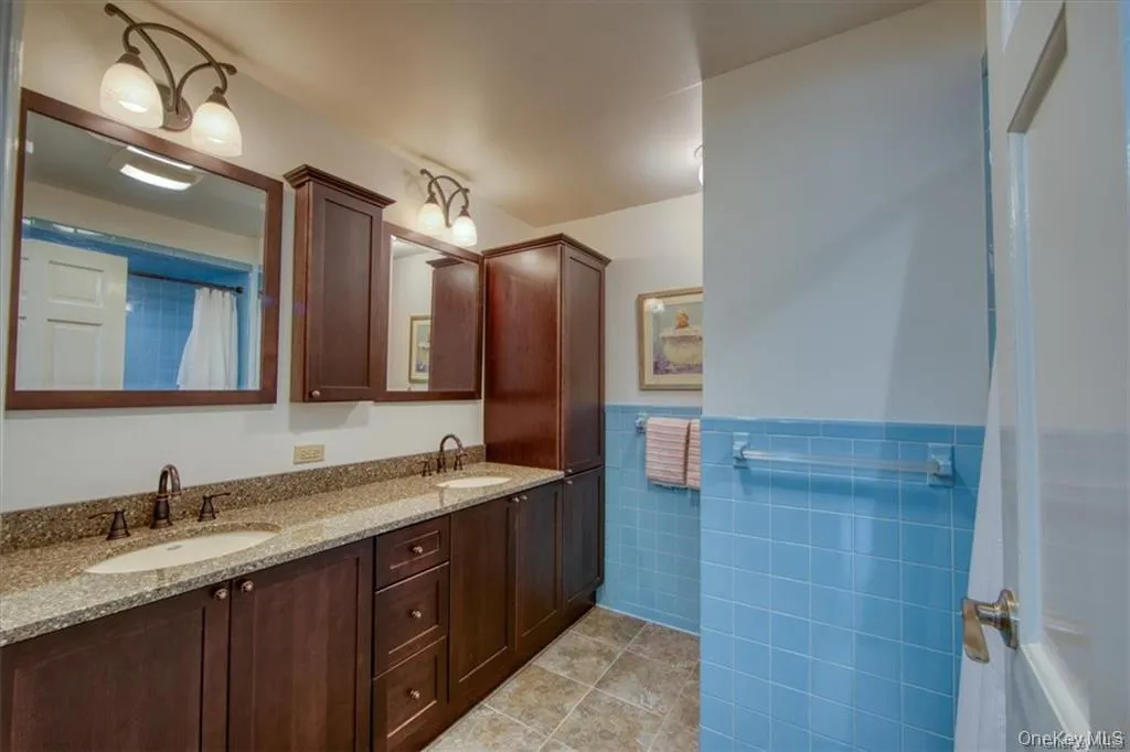 Bathroom featuring double vanity, tile walls, light tile patterned flooring, and wainscoting Bathroom featuring double vanity, tile walls, light tile patterned flooring, and wainscoting