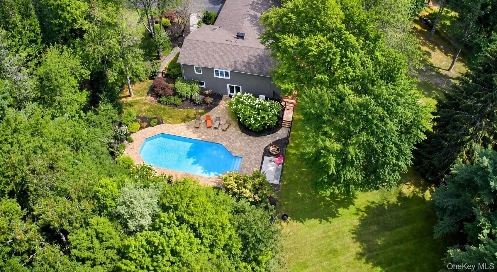 Backyard oasis featuring an in-ground pool with stone coping, extensive patio space, mature trees, and landscaping surrounding the property Backyard oasis featuring an in-ground pool with stone coping, extensive patio space, mature trees, and landscaping surrounding the property