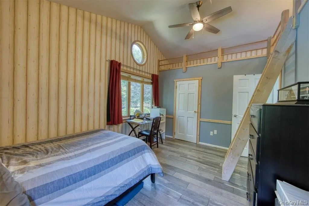 Vaulted ceilings, wood-finish flooring, wood plank accent wall, round transom window, and a ceiling fan Vaulted ceilings, wood-finish flooring, wood plank accent wall, round transom window, and a ceiling fan
