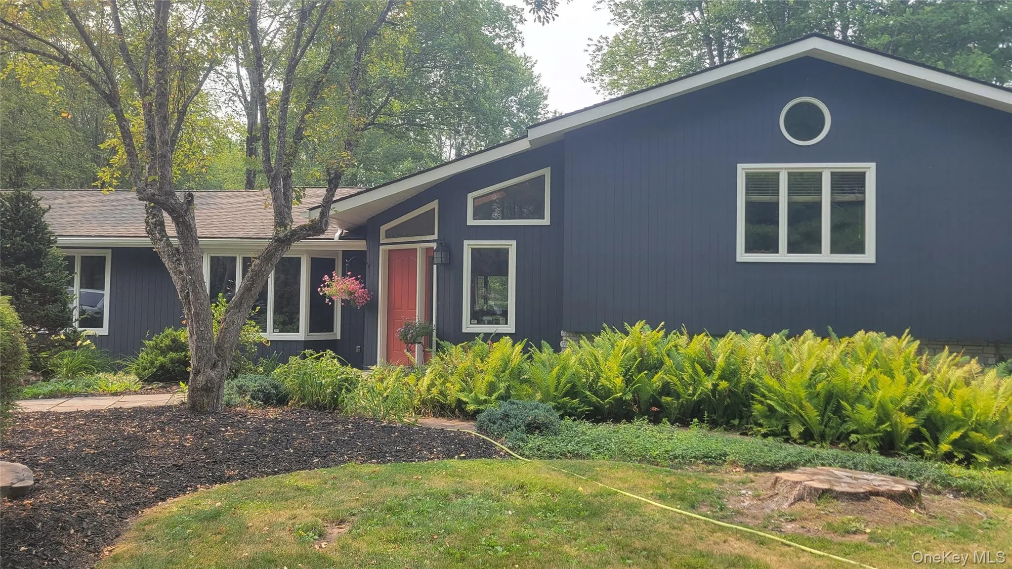 Exterior featuring dark gray siding, multiple window styles including a round accent window, an angled roofline, and an orange entry door Exterior featuring dark gray siding, multiple window styles including a round accent window, an angled roofline, and an orange entry door