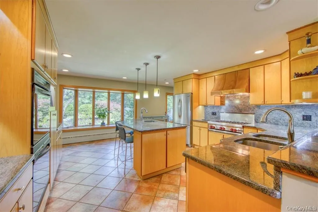 Kitchen featuring light-toned cabinetry, two large kitchen islands with stone countertops, a double-basin sink, and a multi-burner range with a custom hood Kitchen featuring light-toned cabinetry, two large kitchen islands with stone countertops, a double-basin sink, and a multi-burner range with a custom hood