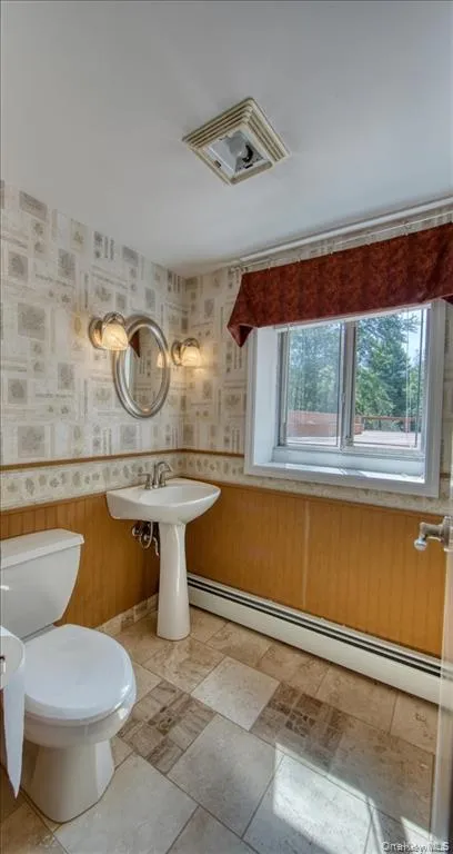 Pedestal sink, wall-mounted light fixtures, window with valance, tiled flooring, and beadboard wainscoting Pedestal sink, wall-mounted light fixtures, window with valance, tiled flooring, and beadboard wainscoting