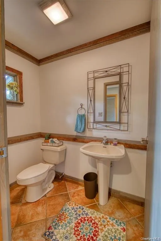 Pedestal sink, ceramic tile flooring, natural wood accents, white toilet, and recessed lighting Pedestal sink, ceramic tile flooring, natural wood accents, white toilet, and recessed lighting
