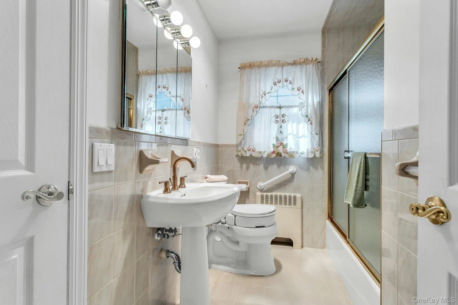 Bathroom with enclosed tub / shower combo, radiator heating unit, light tile patterned floors, tile walls, and wainscoting Bathroom with enclosed tub / shower combo, radiator heating unit, light tile patterned floors, tile walls, and wainscoting