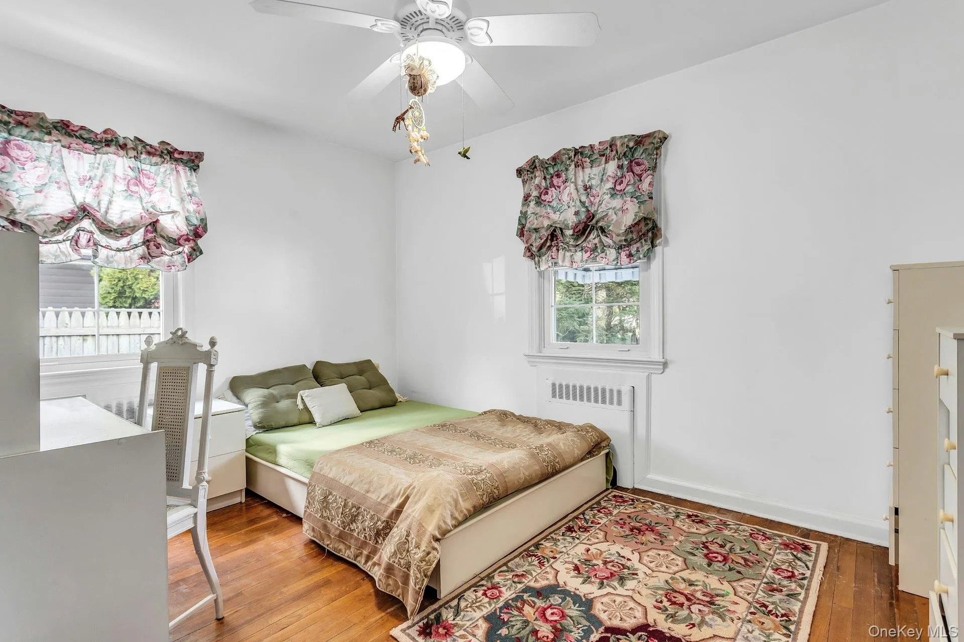 Bedroom featuring radiator heating unit, hardwood / wood-style flooring, ceiling fan, and multiple windows Bedroom featuring radiator heating unit, hardwood / wood-style flooring, ceiling fan, and multiple windows