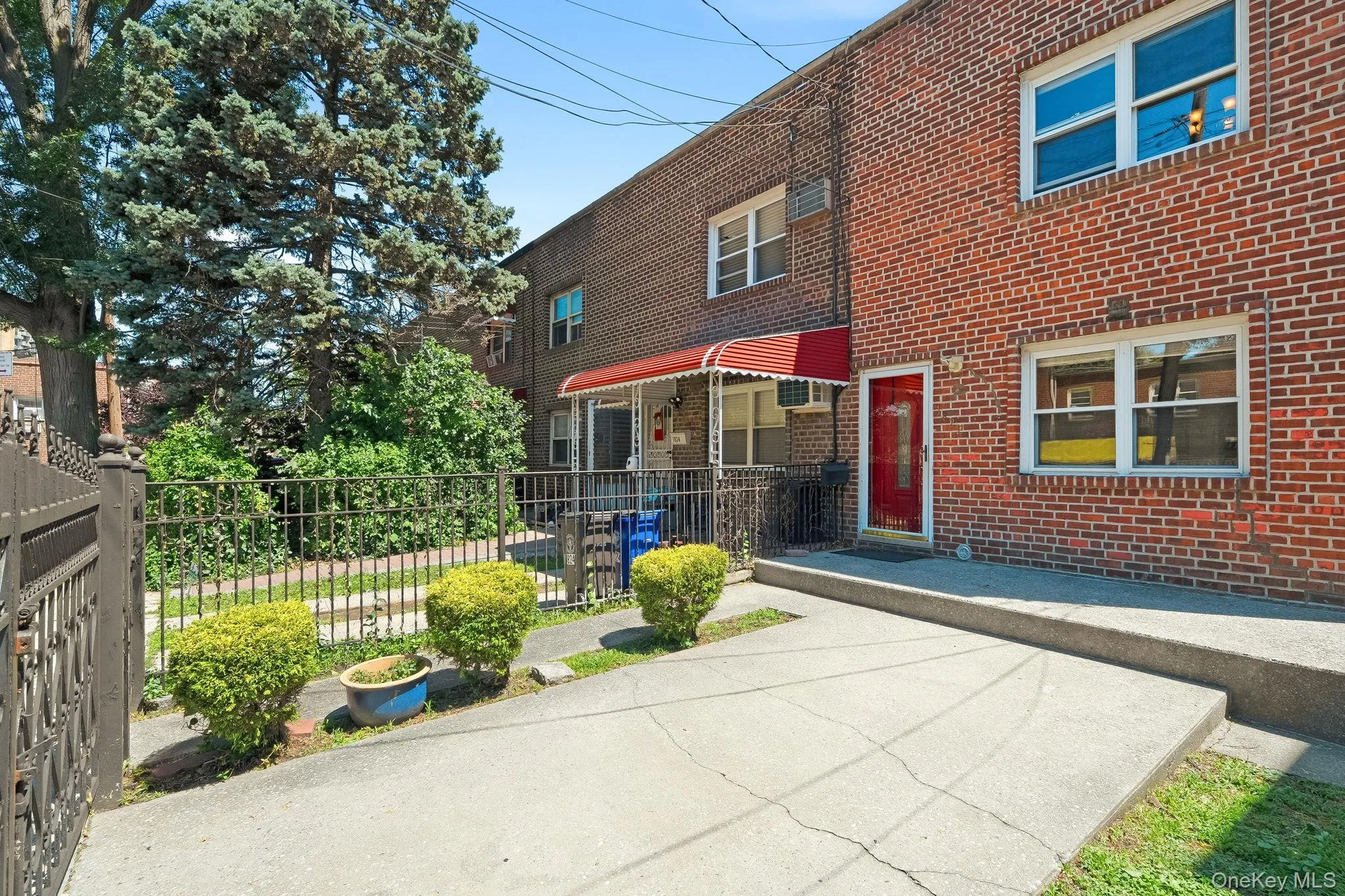 Brick facade exterior featuring a red entry door, a red striped awning, a concrete driveway, and a black wrought iron fence. Brick facade exterior featuring a red entry door, a red striped awning, a concrete driveway, and a black wrought iron fence.