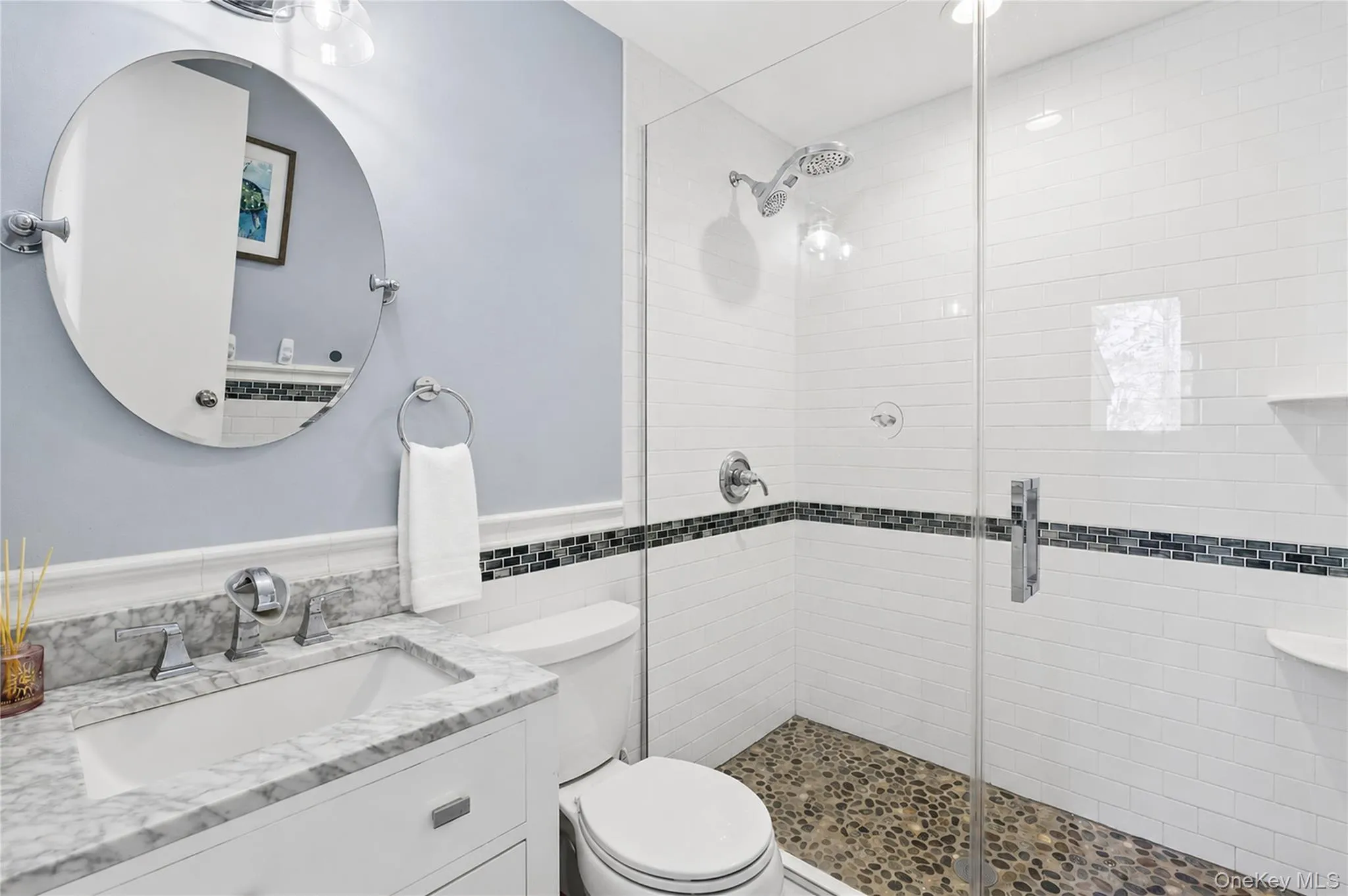 Full bathroom with stone-tiled shower floor and a decorative band of blue, black, and turquoise tiles set within white shower walls. Full bathroom with stone-tiled shower floor and a decorative band of blue, black, and turquoise tiles set within white shower walls.