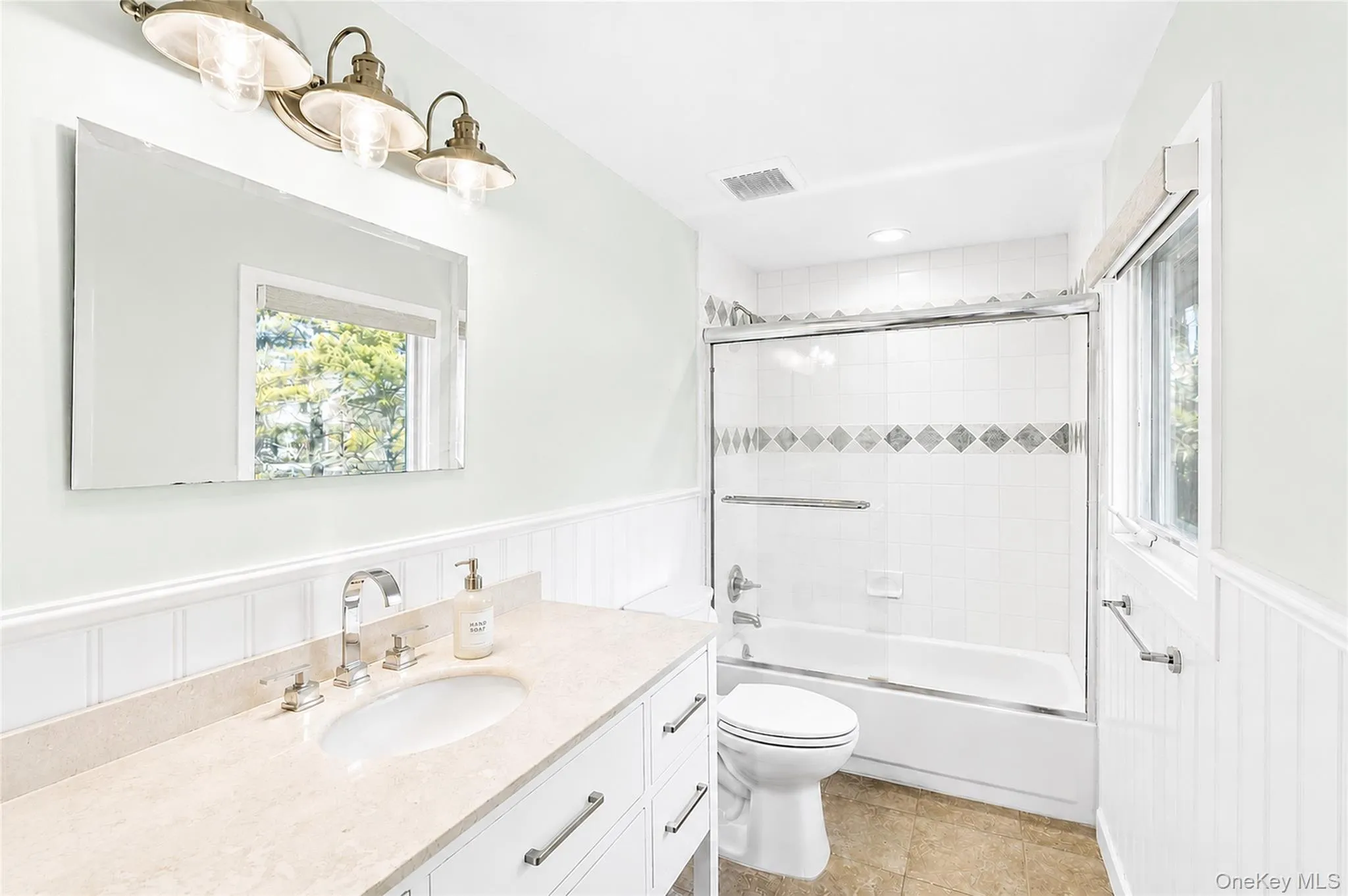 Full bathroom with a bathtub and decorative tile accents set within white wall tile. Full bathroom with a bathtub and decorative tile accents set within white wall tile.