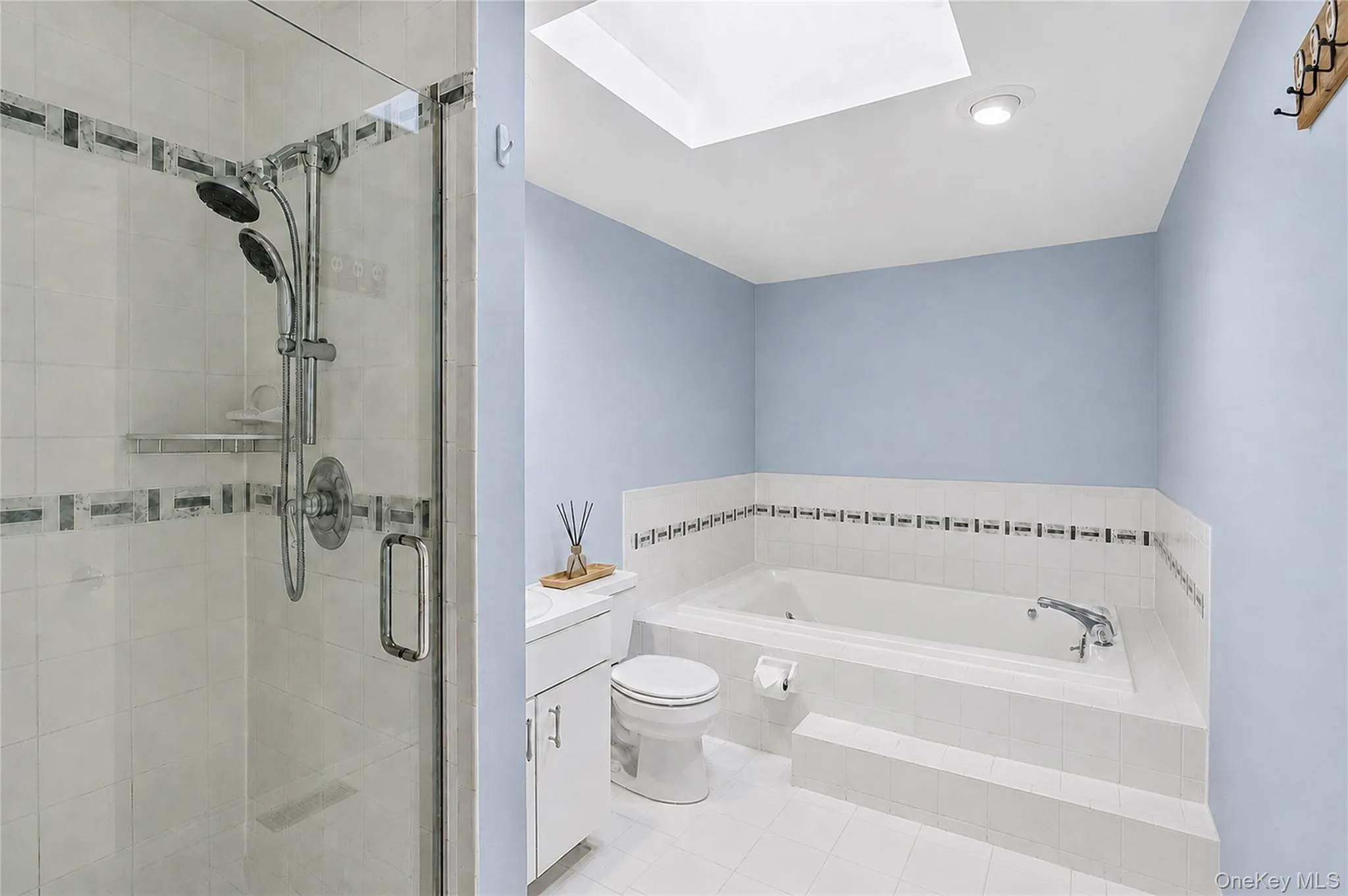 Primary bathroom featuring a soaking tub with jets, skylight, separate shower, and decorative tile work. Primary bathroom featuring a soaking tub with jets, skylight, separate shower, and decorative tile work.