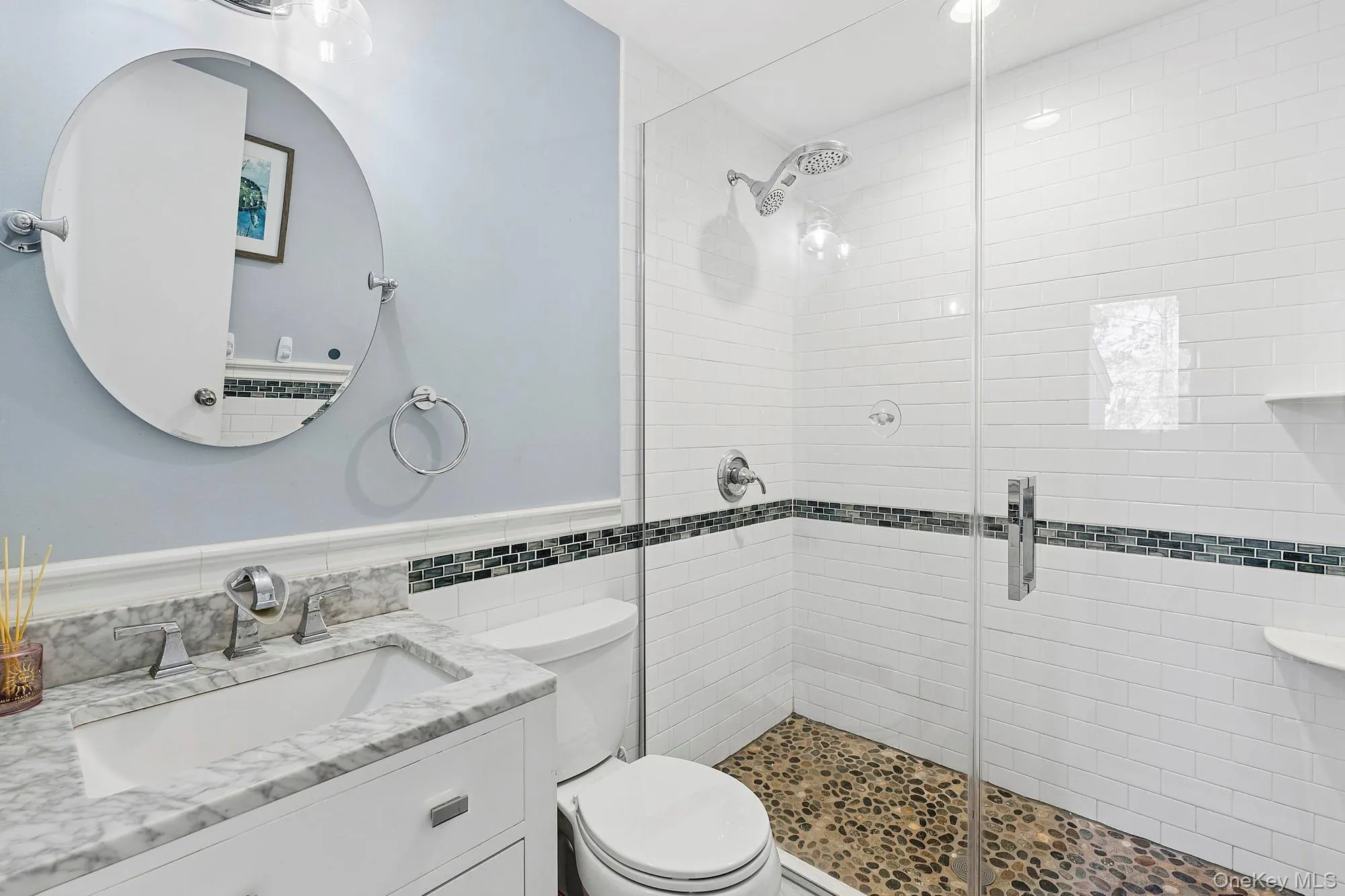 Full bathroom with stone-tiled shower floor and a decorative band of blue, black, and turquoise tiles set within white shower walls. Full bathroom with stone-tiled shower floor and a decorative band of blue, black, and turquoise tiles set within white shower walls.