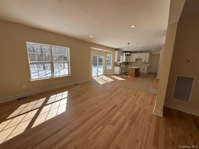 Unfurnished living room featuring light wood-style floors and hanging lights Unfurnished living room featuring light wood-style floors and hanging lights