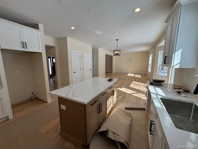 Two tone kitchen featuring light wood-type flooring, a kitchen island, light stone counters, a chandelier, and open floor plan Two tone kitchen featuring light wood-type flooring, a kitchen island, light stone counters, a chandelier, and open floor plan