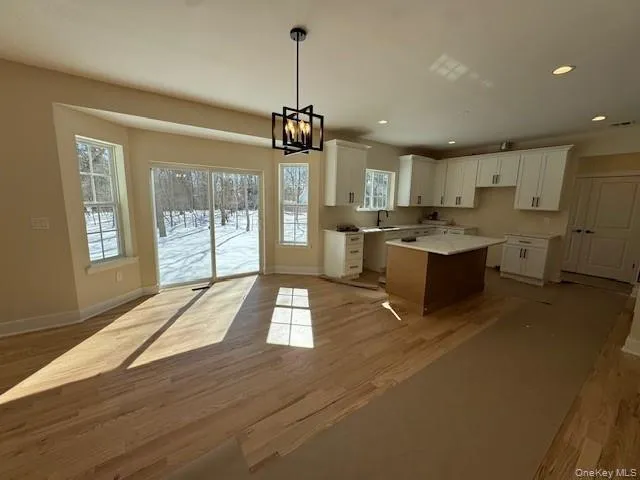 Kitchen featuring hanging lights, white cabinetry, light wood finished floors, and a kitchen island Kitchen featuring hanging lights, white cabinetry, light wood finished floors, and a kitchen island
