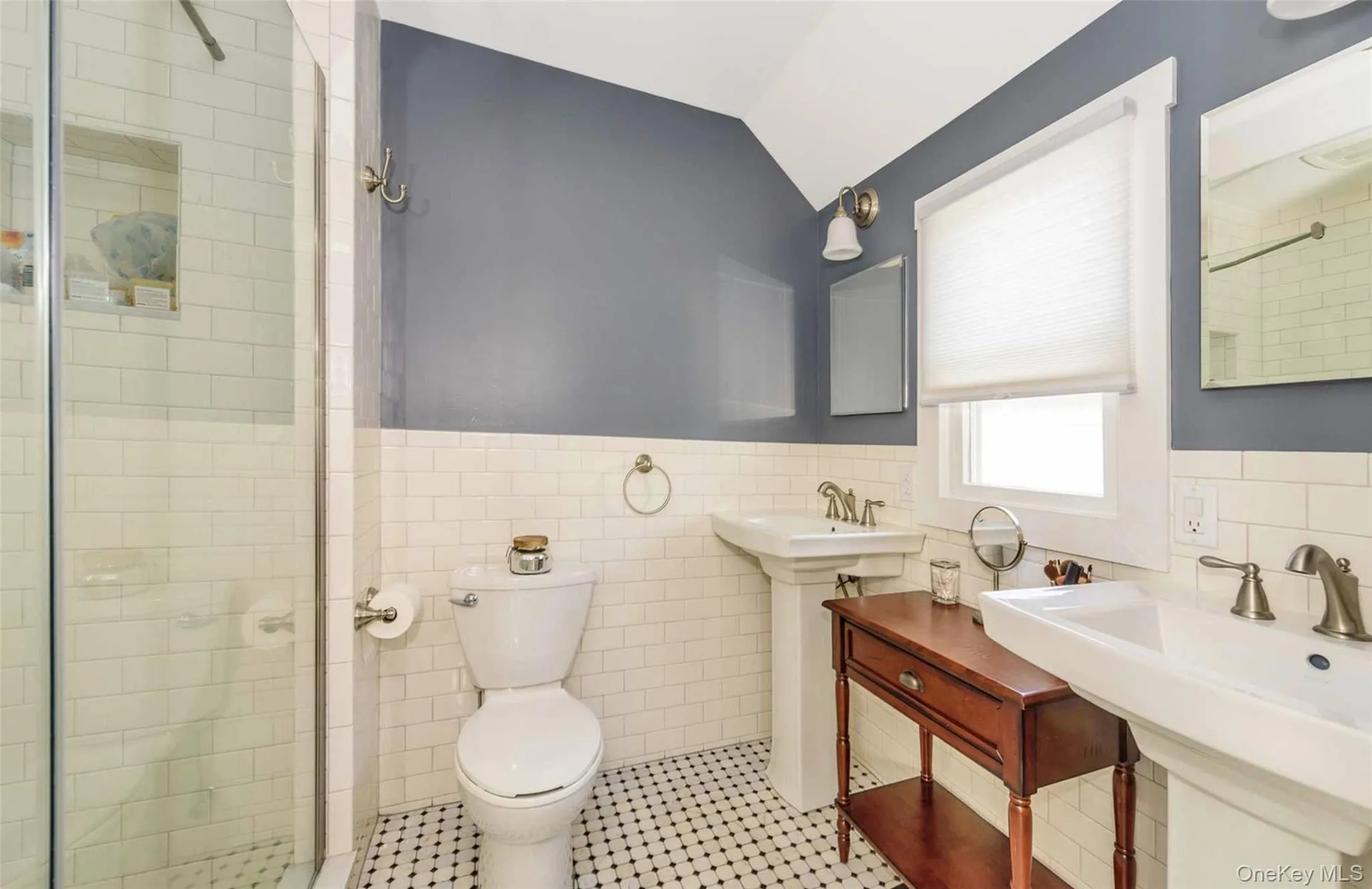 Bathroom featuring vaulted ceiling, sink, tiled shower, tile walls, and toilet Bathroom featuring vaulted ceiling, sink, tiled shower, tile walls, and toilet