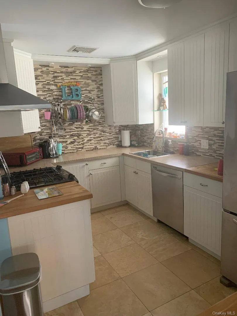 Kitchen with decorative backsplash, wall chimney exhaust hood, light tile patterned floors, and stainless steel appliances Kitchen with decorative backsplash, wall chimney exhaust hood, light tile patterned floors, and stainless steel appliances