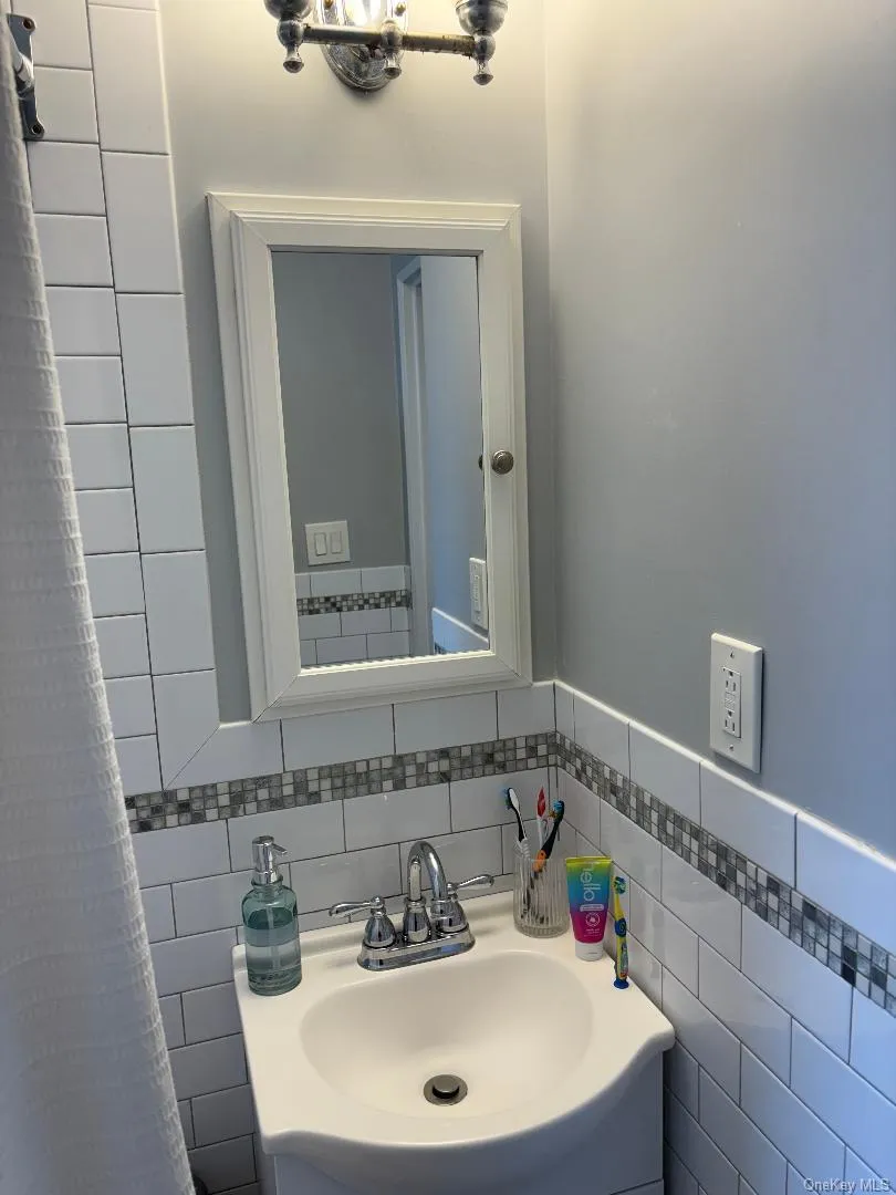 Bathroom featuring vanity, tasteful backsplash, and tile walls Bathroom featuring vanity, tasteful backsplash, and tile walls